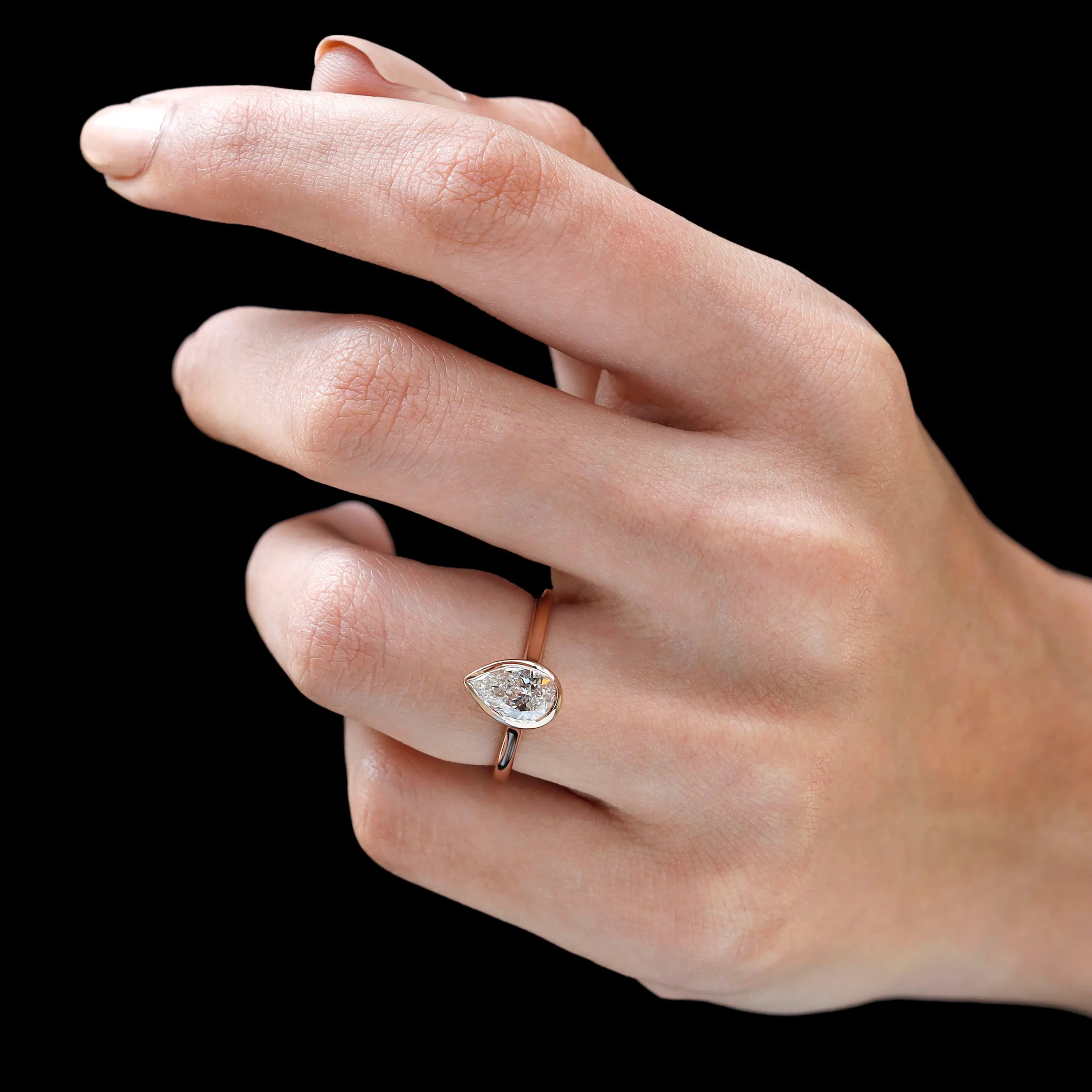 Pear cut bezel cathedral diamond ring worn on hand angled view
