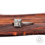 Angled view of princess cut bezel set diamond ring on wooden surface