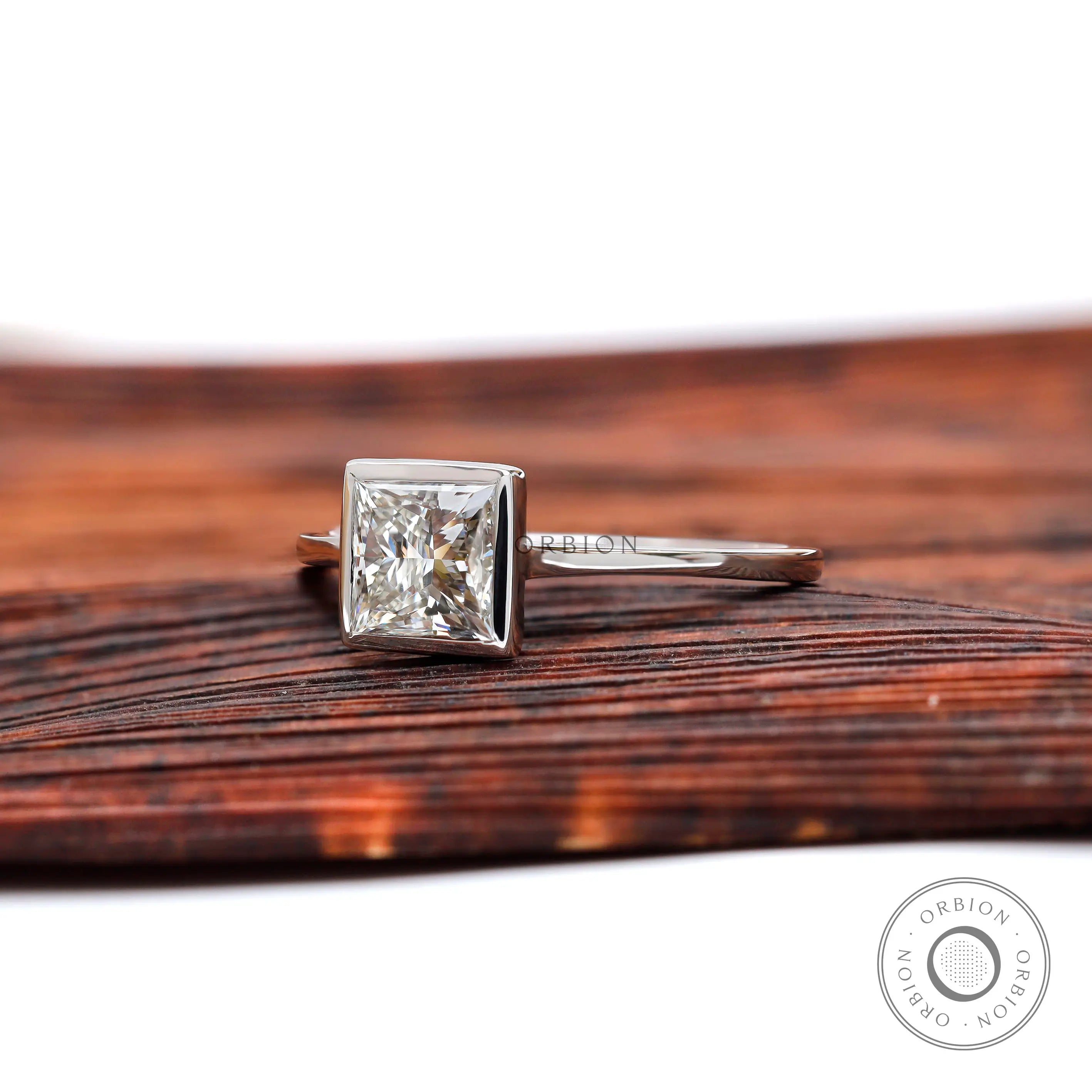 Angled view of princess cut bezel set diamond ring on wooden surface