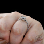 Princess cut diamond ring held between fingers for scale