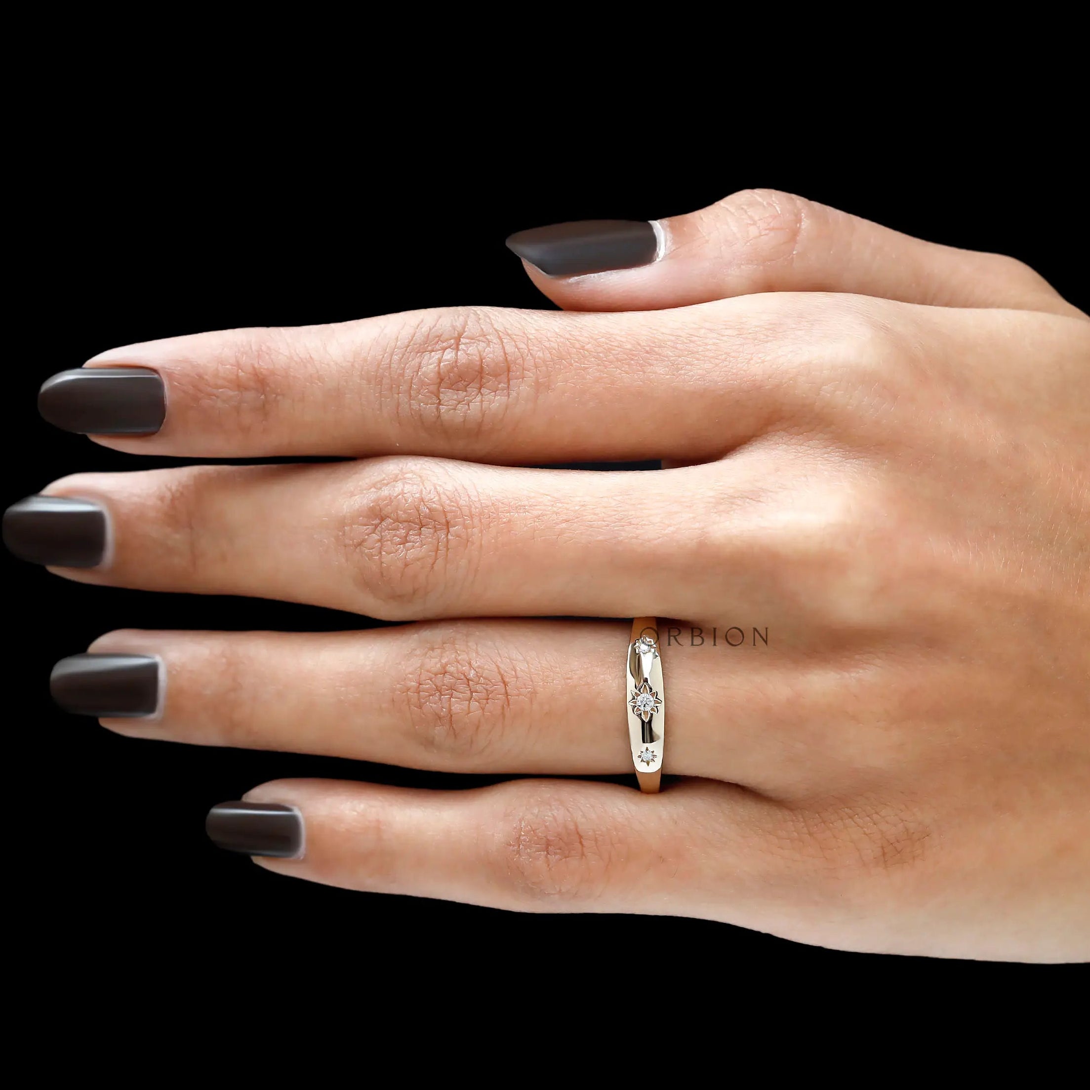 Hand view of polished yellow gold diamond band with starburst details.