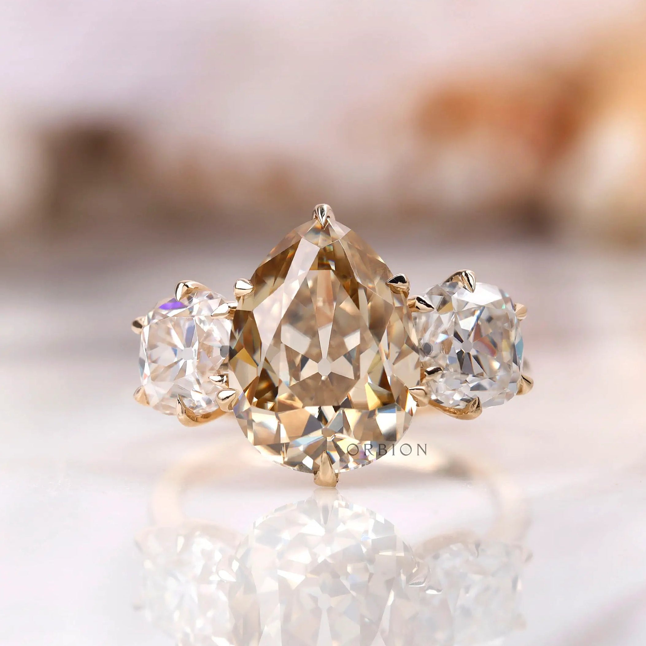 Light champagne pear old mine cut moissanite three stone ring in yellow gold