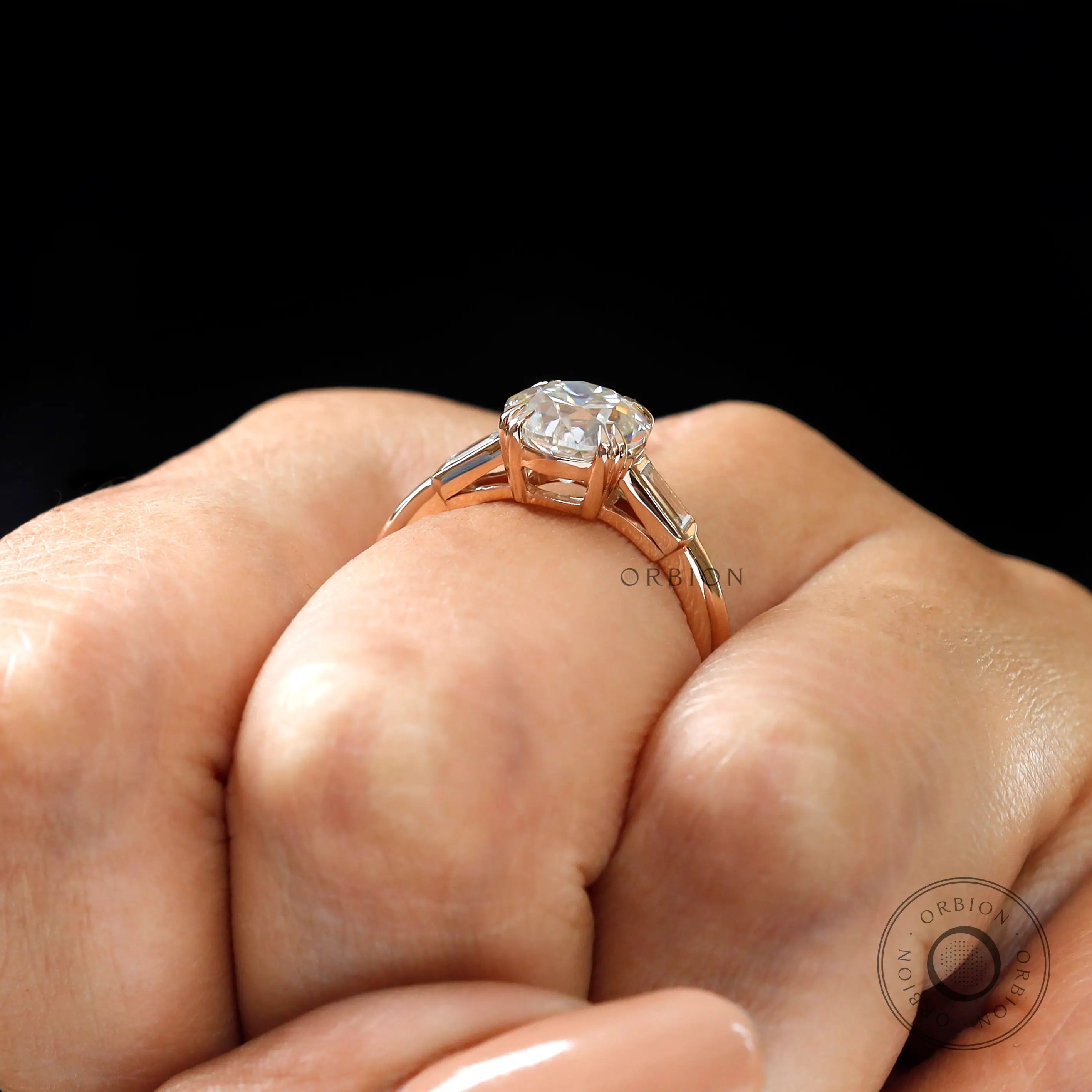 Close-up shot of Moissanite three-stone round Old European cut ring with baguette side stones on a hand