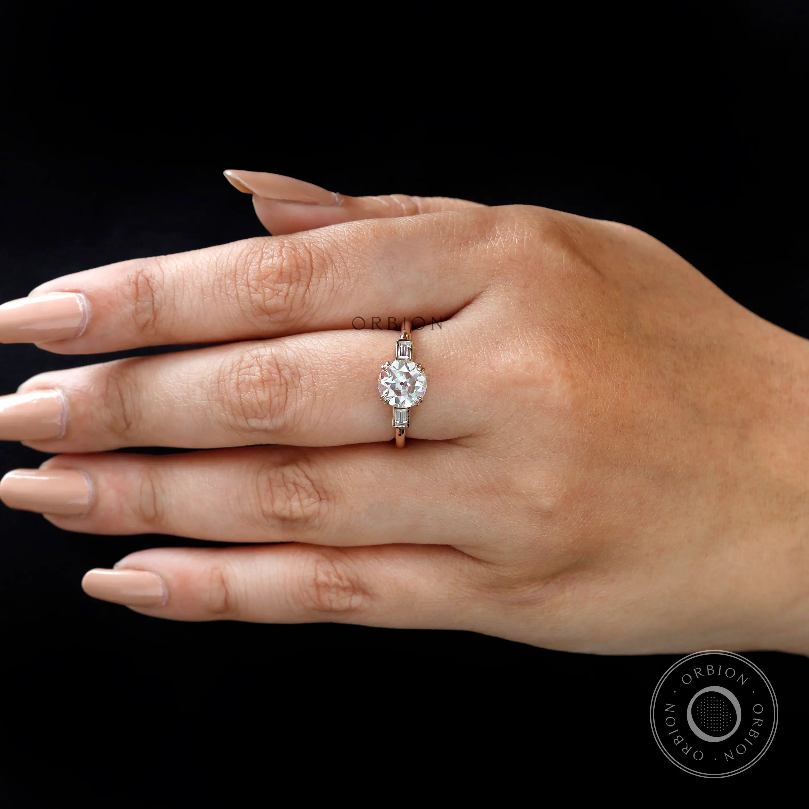 Hand wearing Moissanite three-stone round Old European cut engagement ring with baguette side stones in 10K yellow gold