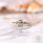 Moissanite engagement ring with square cushion center stone and round brilliant-cut side stones in 10K yellow gold.