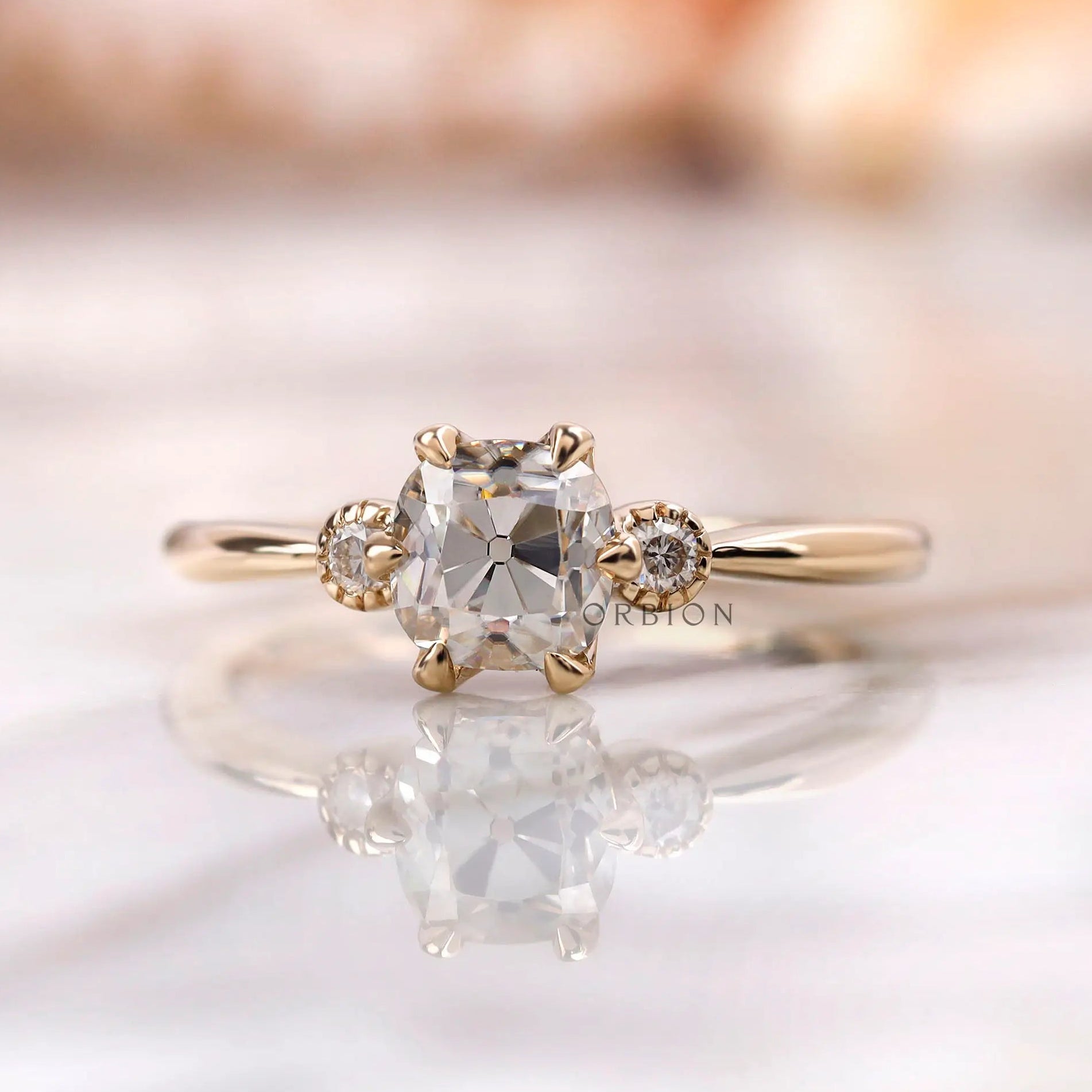 Moissanite engagement ring with square cushion center stone and round brilliant-cut side stones in 10K yellow gold.