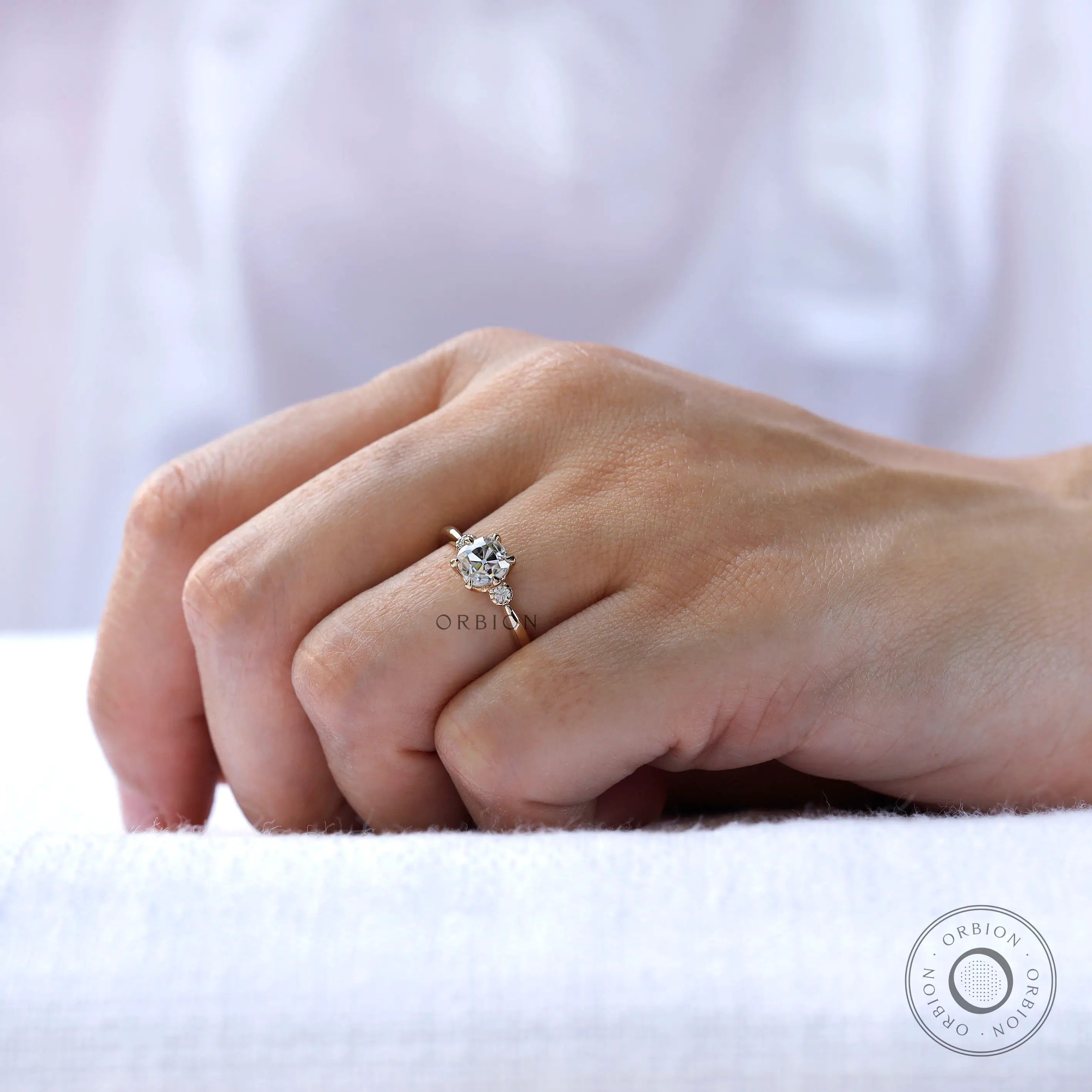 Moissanite engagement ring with a round brilliant-cut side stone, showing its high-polish finish and tapered band.