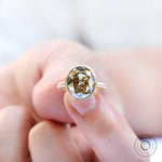 Bezel set oval champagne ring held close-up
