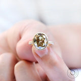 Bezel set oval champagne ring held close-up