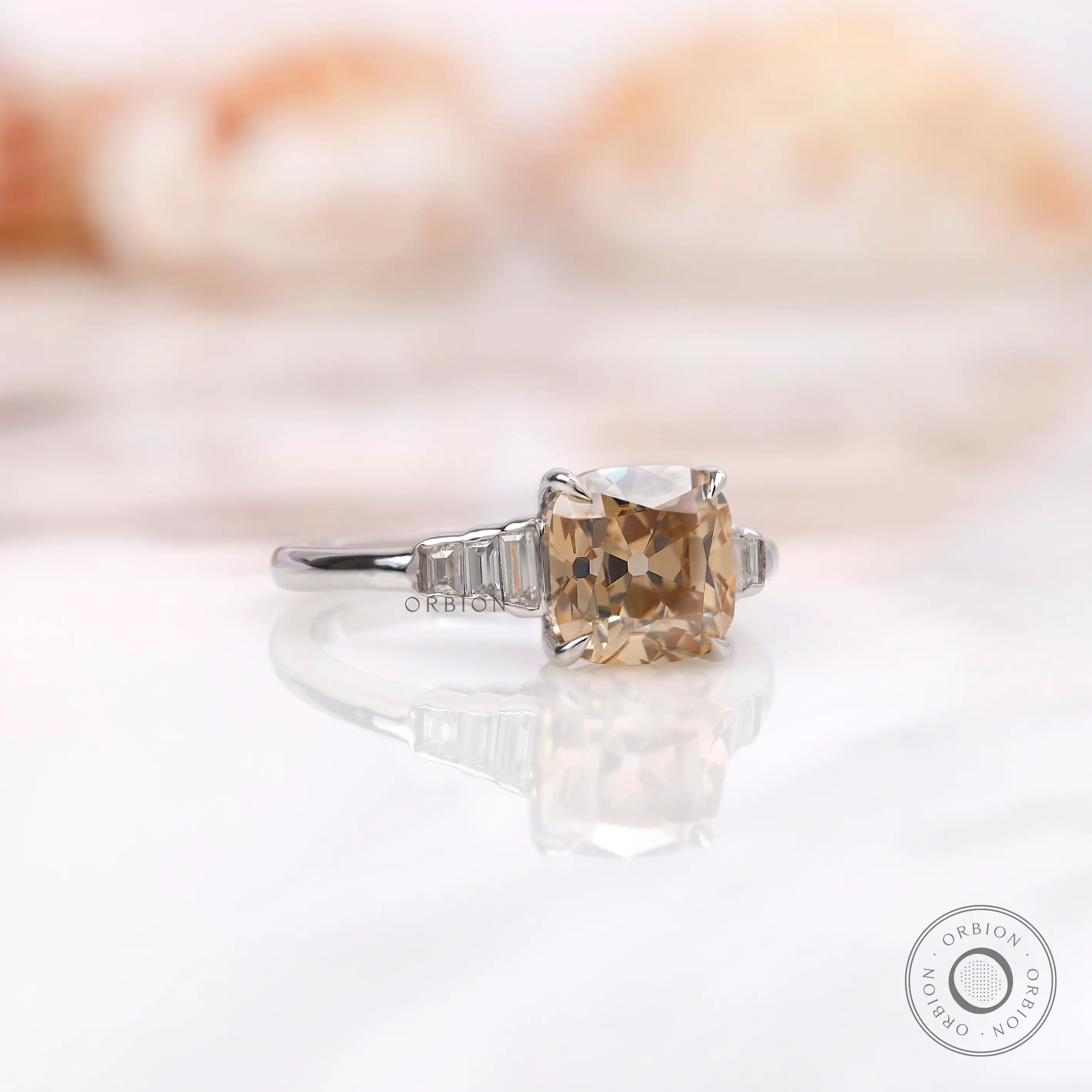 A close-up side view of a champagne cushion moissanite ring with baguette side stones.