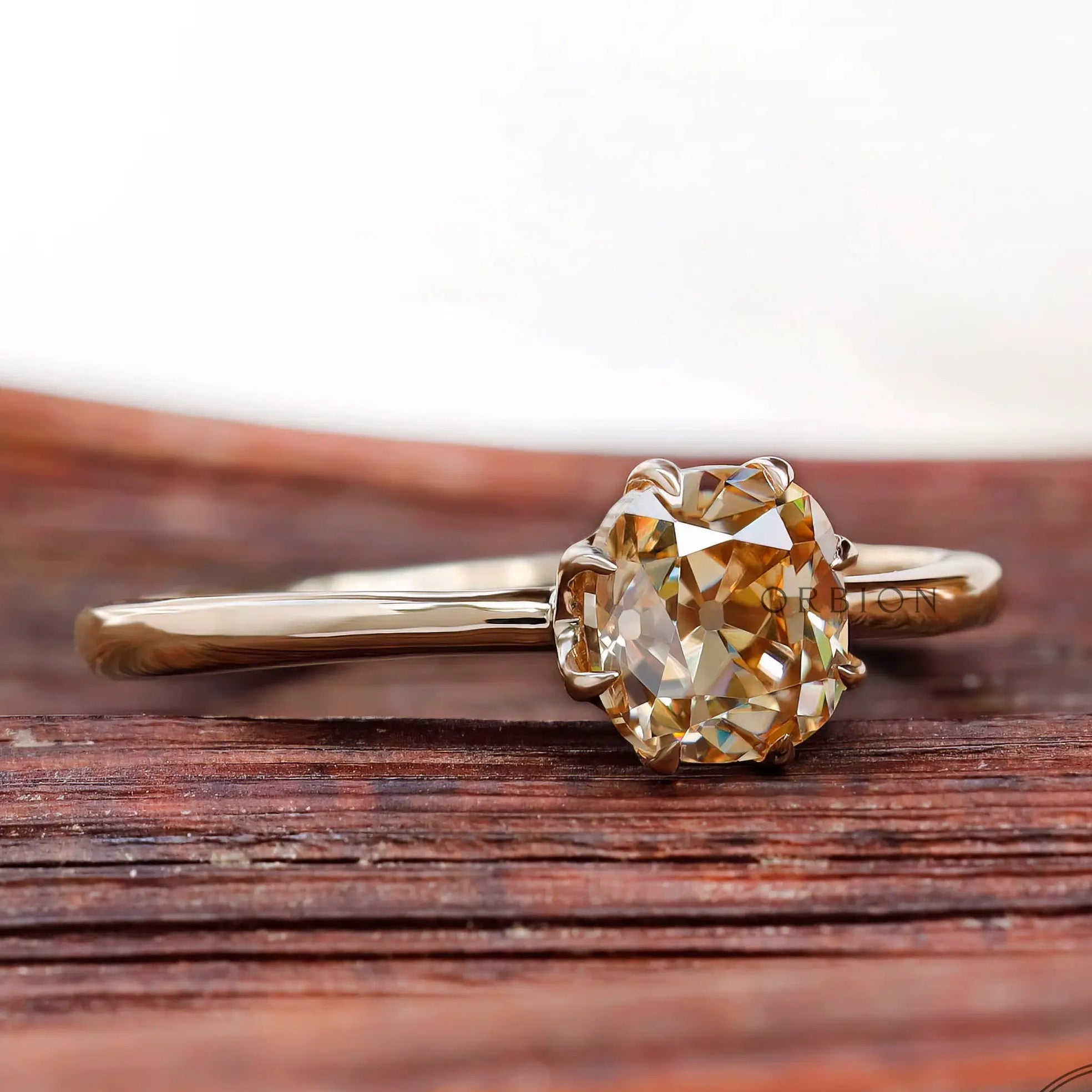 Champagne Moissanite solitaire ring with simple band, angled view on wood