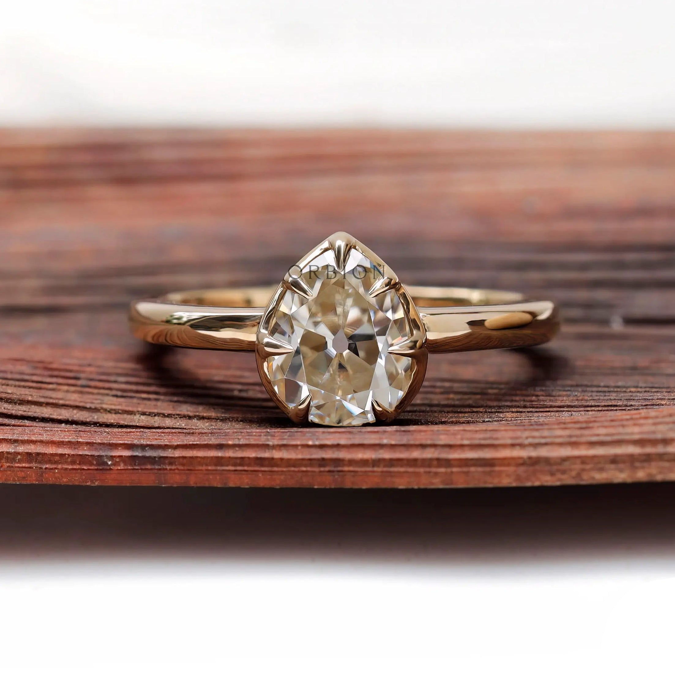 Pear moissanite solitaire ring shown front on wood