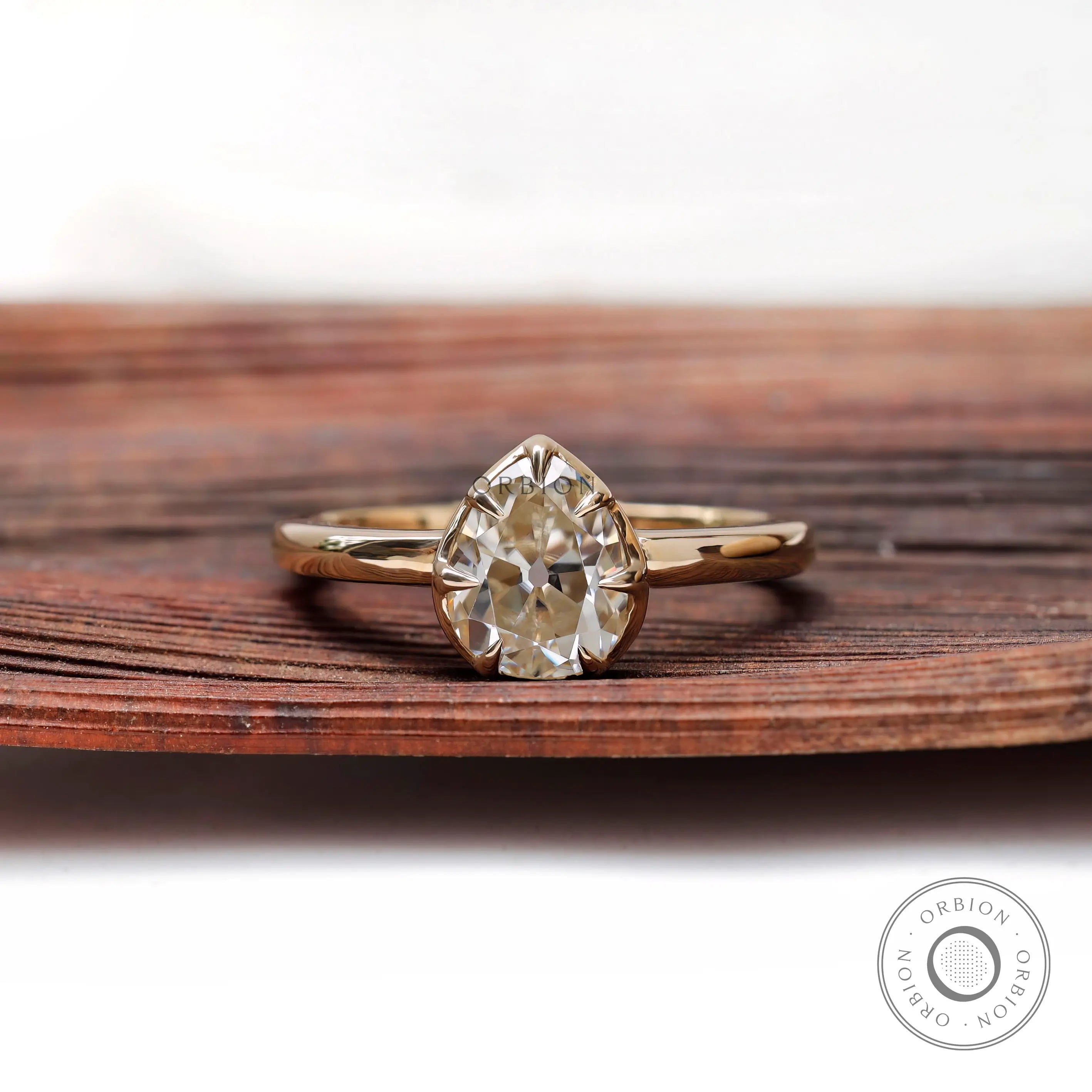 Pear moissanite solitaire ring shown front on wood