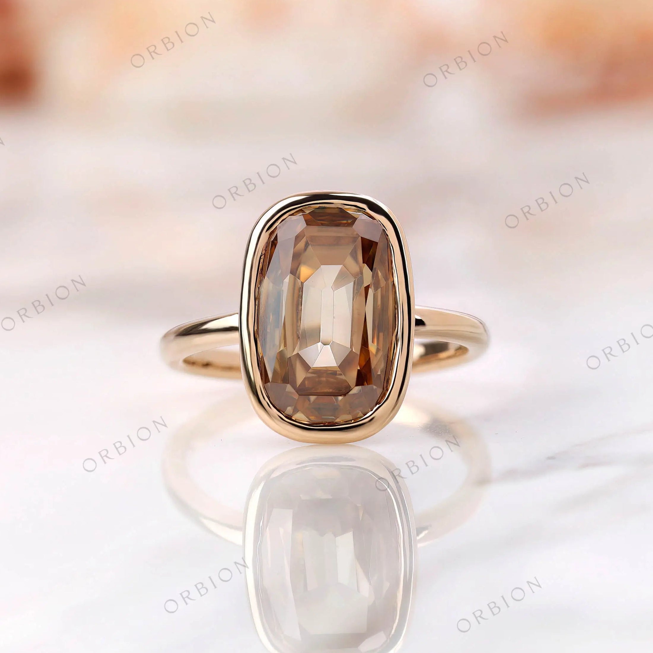 Front view of elongated cushion champagne moissanite bezel ring in yellow gold.