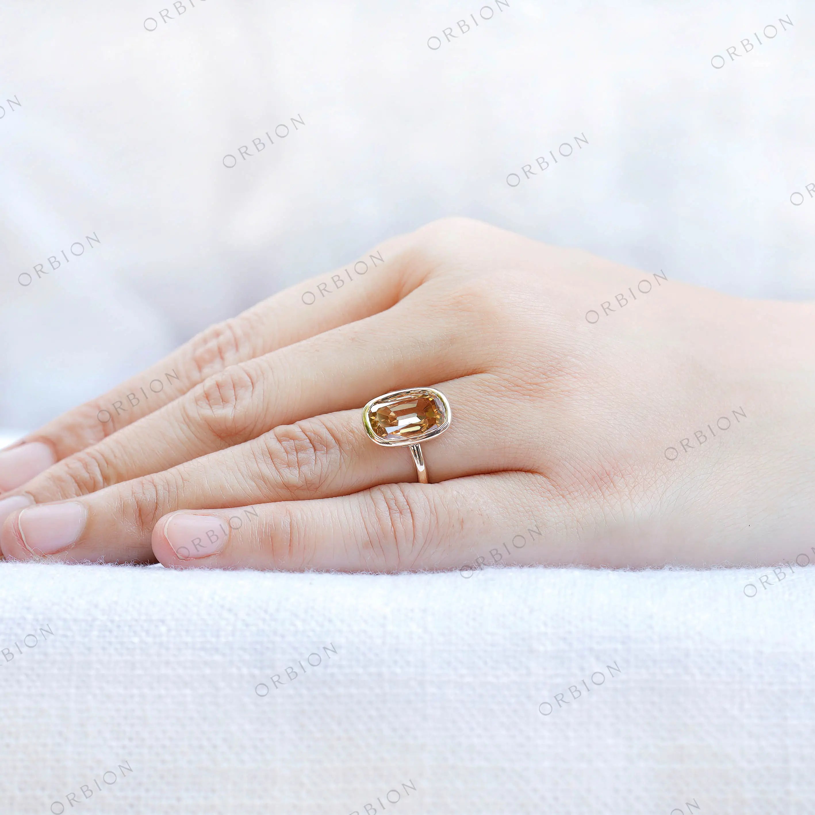Elongated cushion champagne moissanite bezel ring in yellow gold worn on hand.