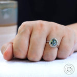 Oval bluish green moissanite halo ring worn on finger