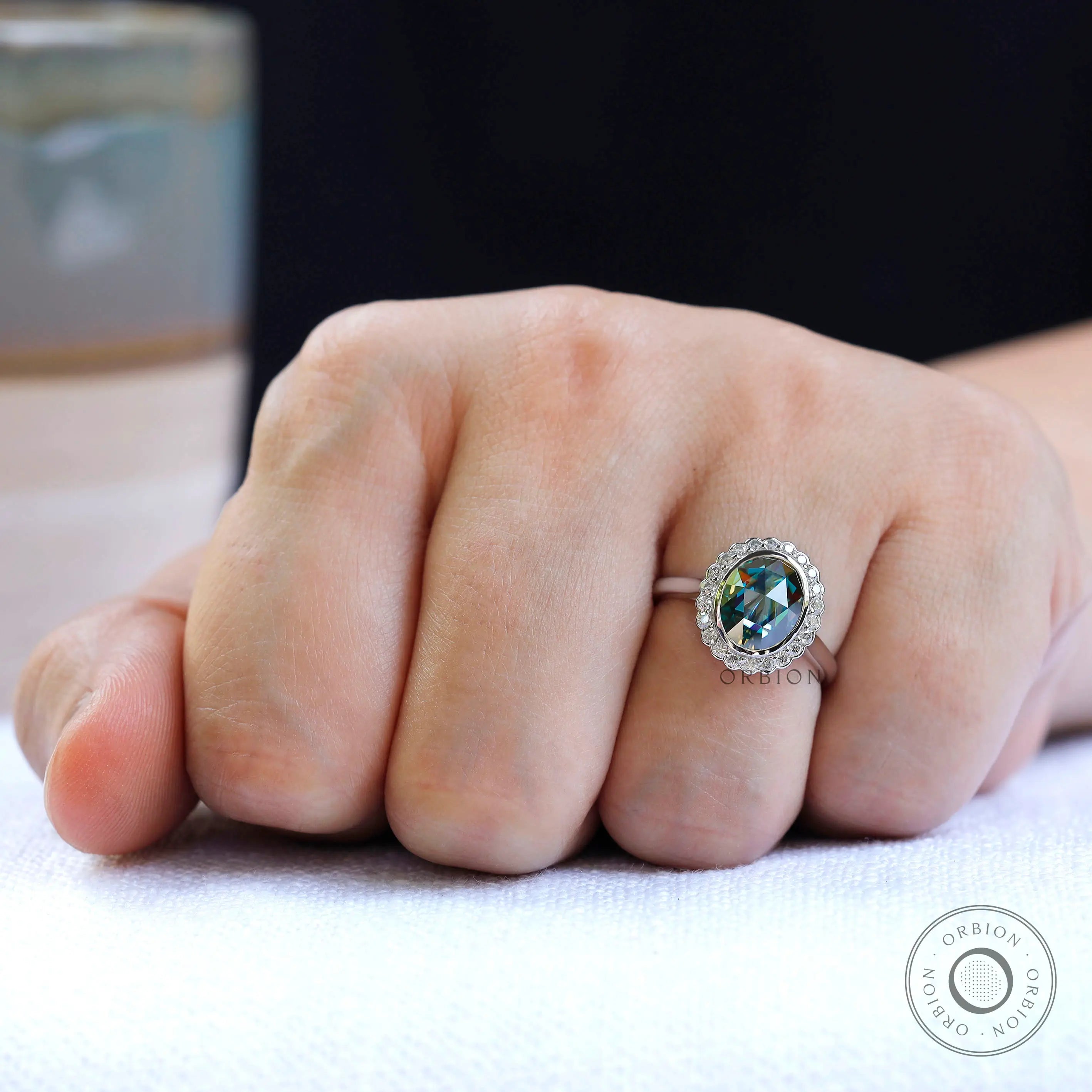 Oval bluish green moissanite halo ring worn on finger