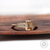 Close view of emerald cut champagne moissanite ring with tapered baguette accents