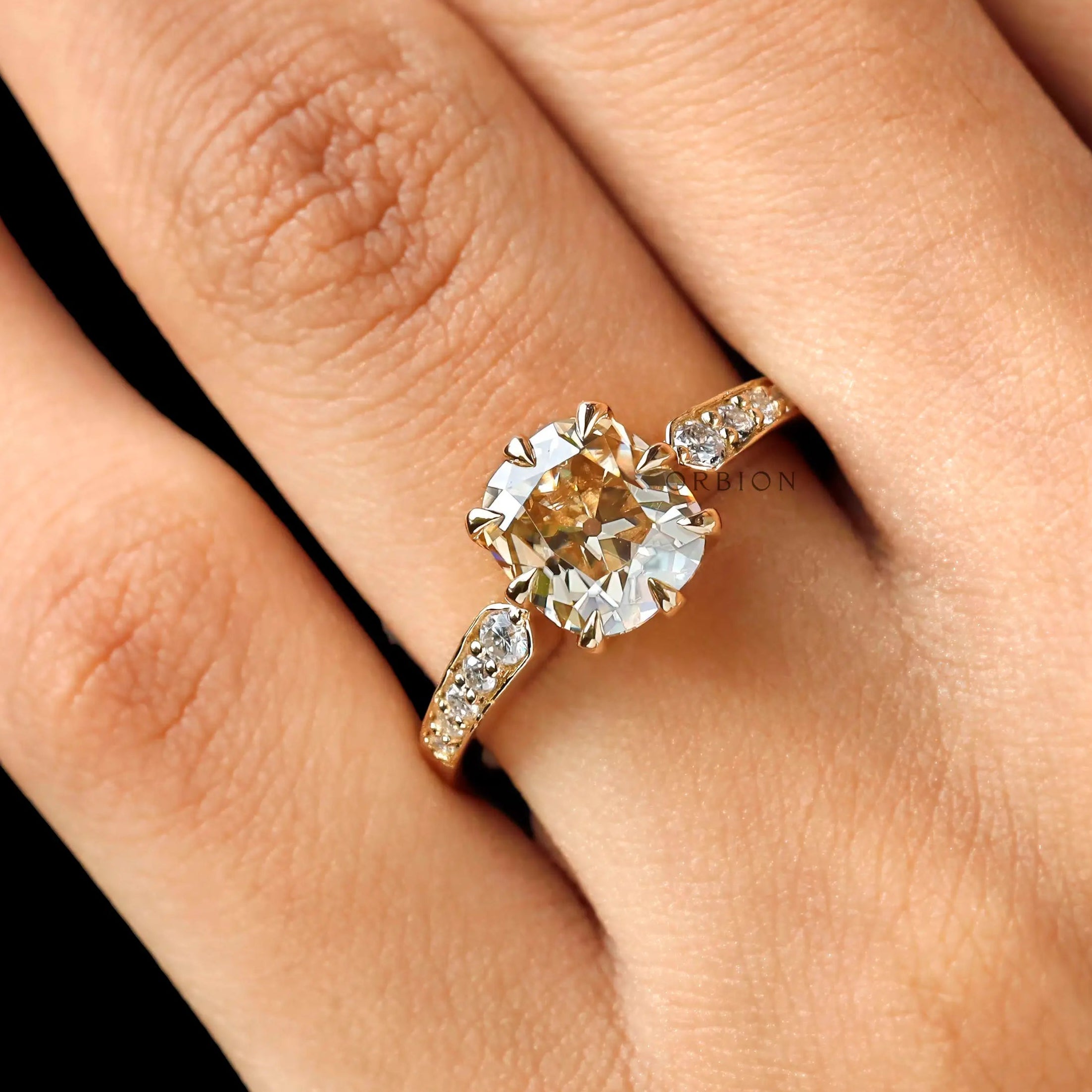 Moissanite engagement ring with an elongated cushion cut center stone, surrounded by round brilliant cut side stones in 18K yellow gold.