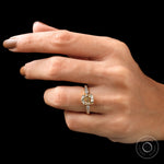 Moissanite engagement ring with elongated cushion cut center stone in 18K yellow gold, worn on the finger.
