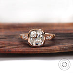 Moissanite engagement ring with elongated cushion center stone and round brilliant side stones in 10K rose gold.