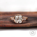 Moissanite engagement ring with elongated cushion center stone and round brilliant side stones in 10K rose gold.