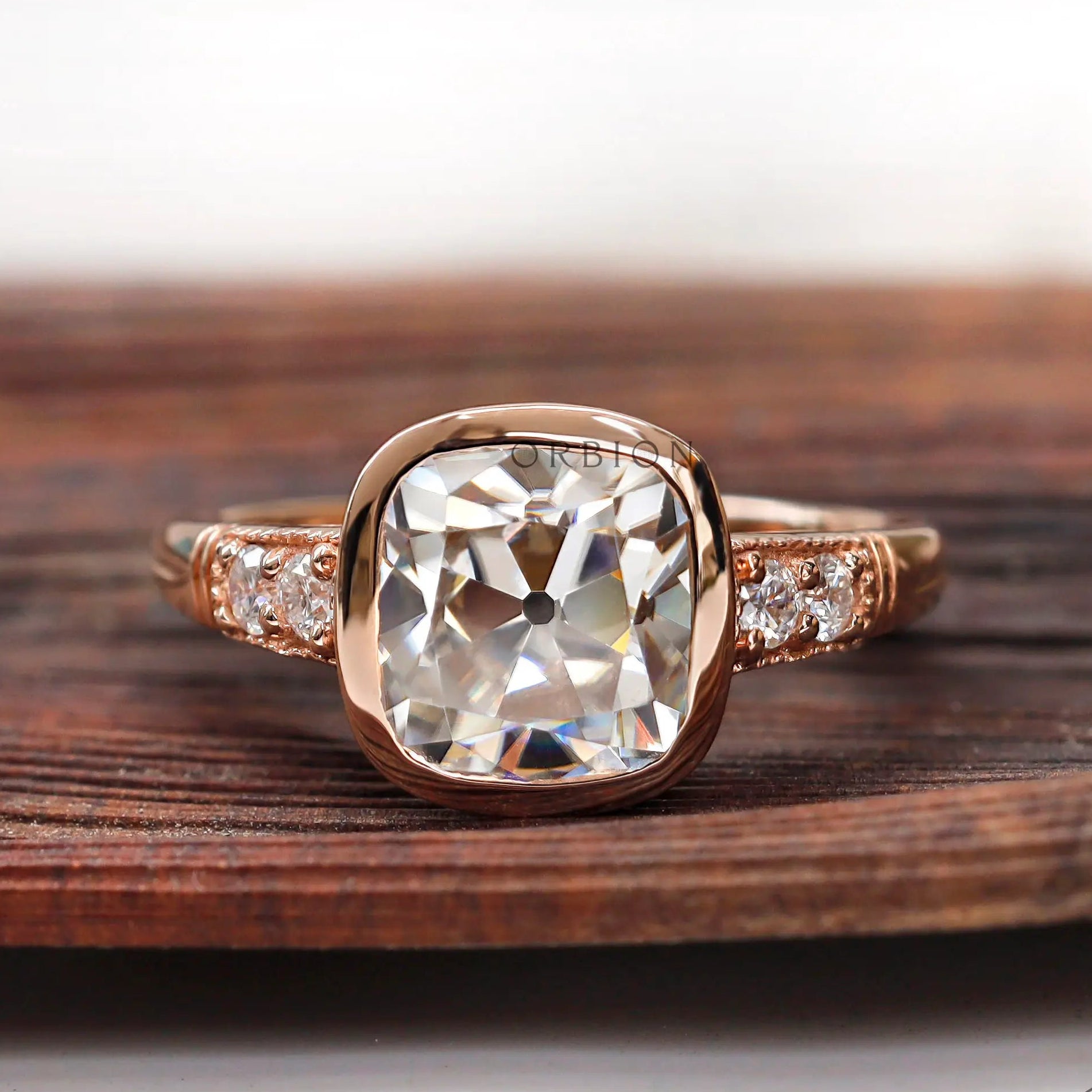 Moissanite engagement ring with elongated cushion center stone and round brilliant side stones in 10K rose gold.