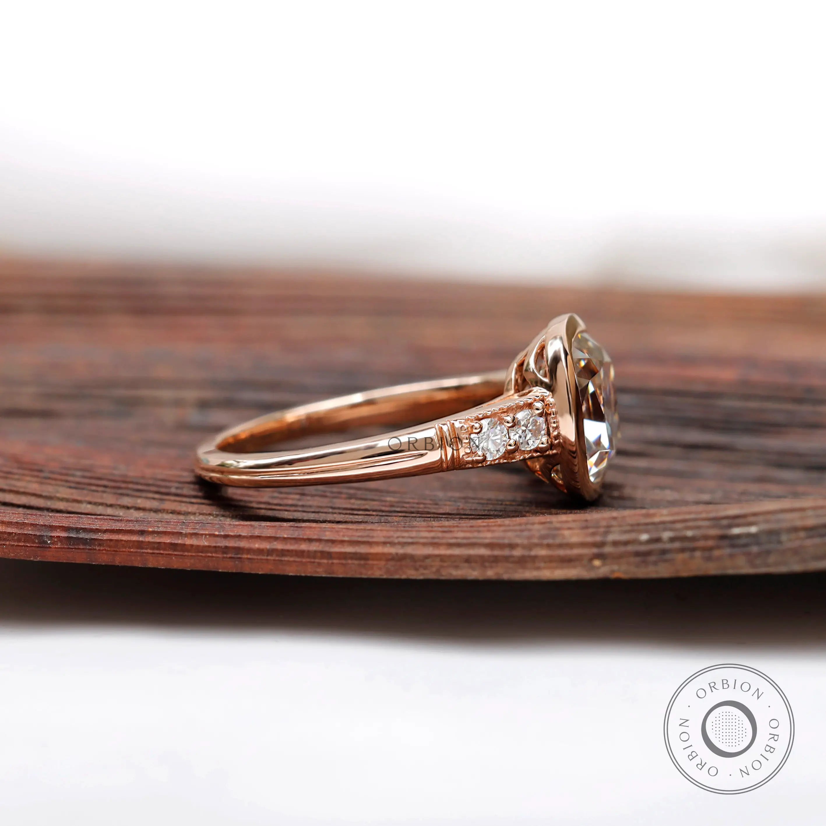 Side view of the engagement ring with elongated cushion moissanite center stone and brilliant-cut side stones in 10K rose gold.