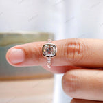 Moissanite engagement ring held by hand, highlighting the elongated cushion center stone and rose gold band.