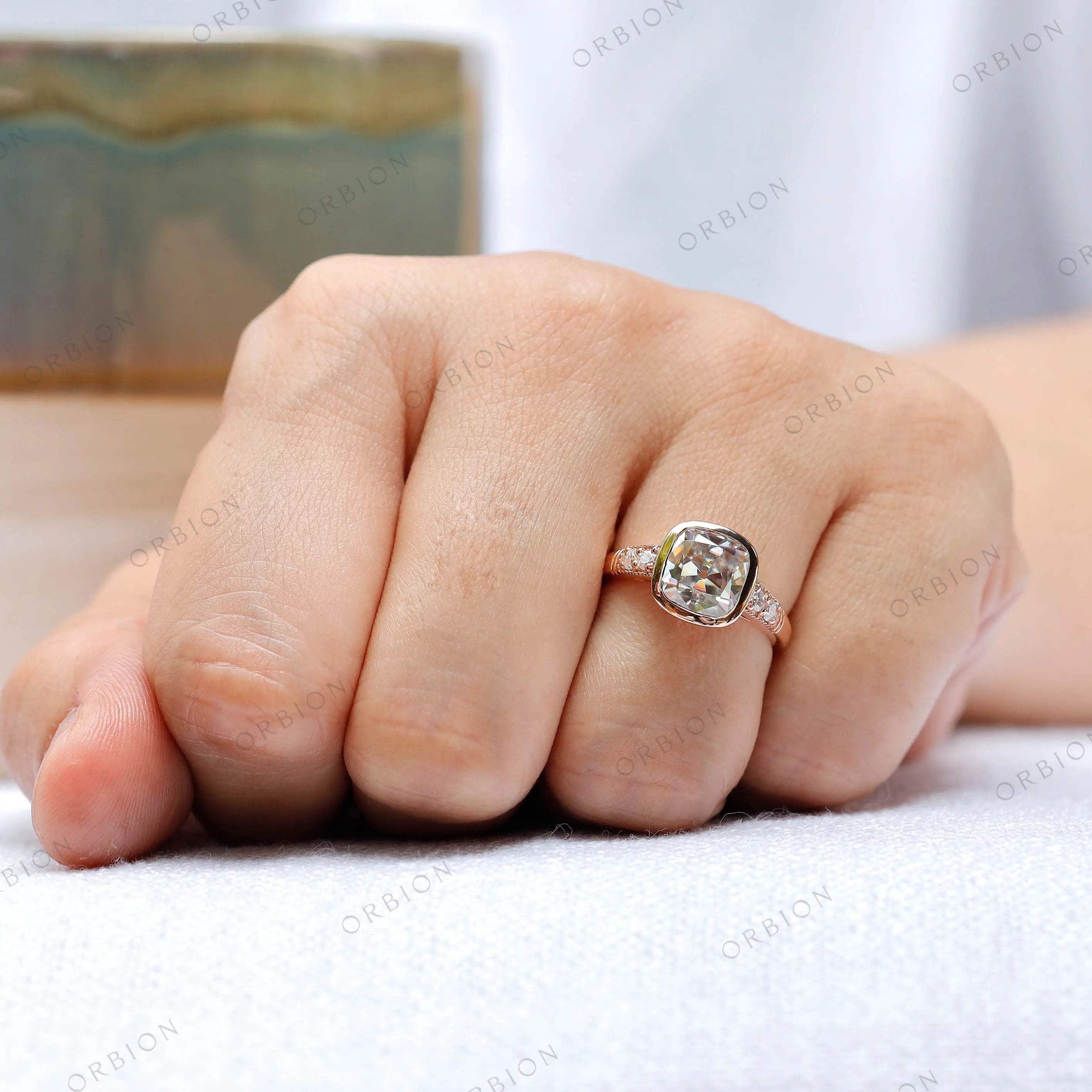 Ring shown on hand, featuring the elongated cushion moissanite center stone and round brilliant-cut side stones in 10K rose gold.