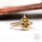 Angled view of pear champagne moissanite ring with round side stones