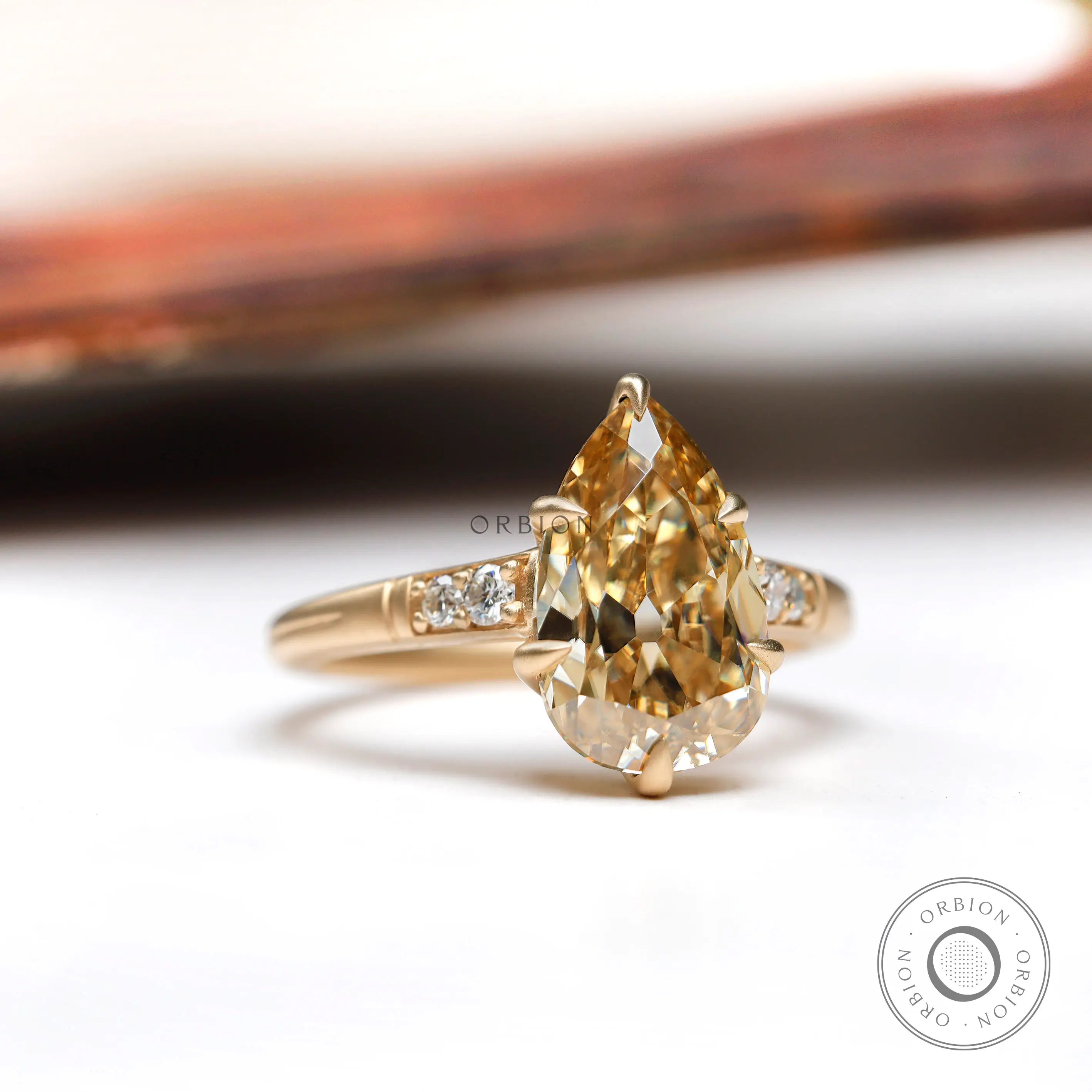 Angled view of pear champagne moissanite ring with round side stones