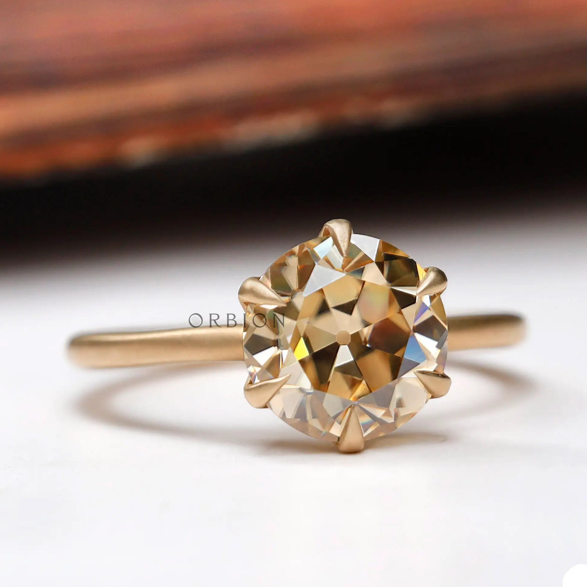 Angled side view of the round Old European Cut light champagne moissanite solitaire engagement ring in yellow gold.