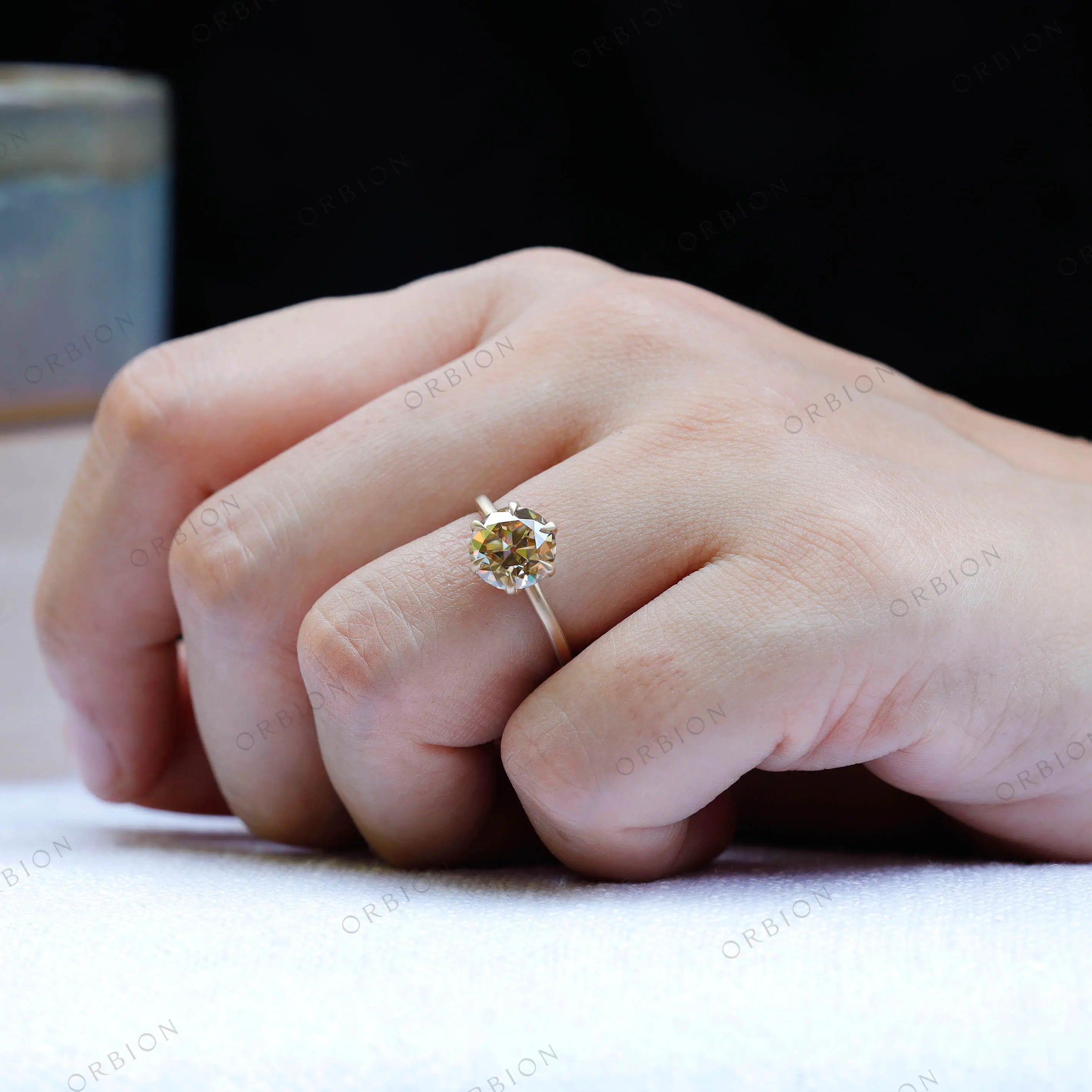 Solitaire round moissanite engagement ring in 10K yellow gold worn on hand.