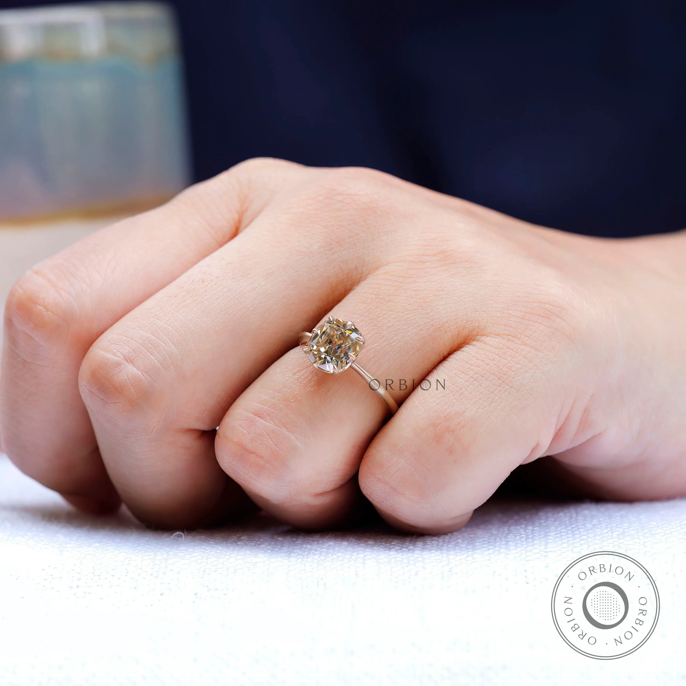 Side angle of hand with OMC cushion champagne moissanite solitaire ring in gold.