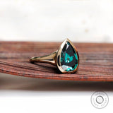 Front view of pear dark green moissanite bezel signet ring in yellow gold