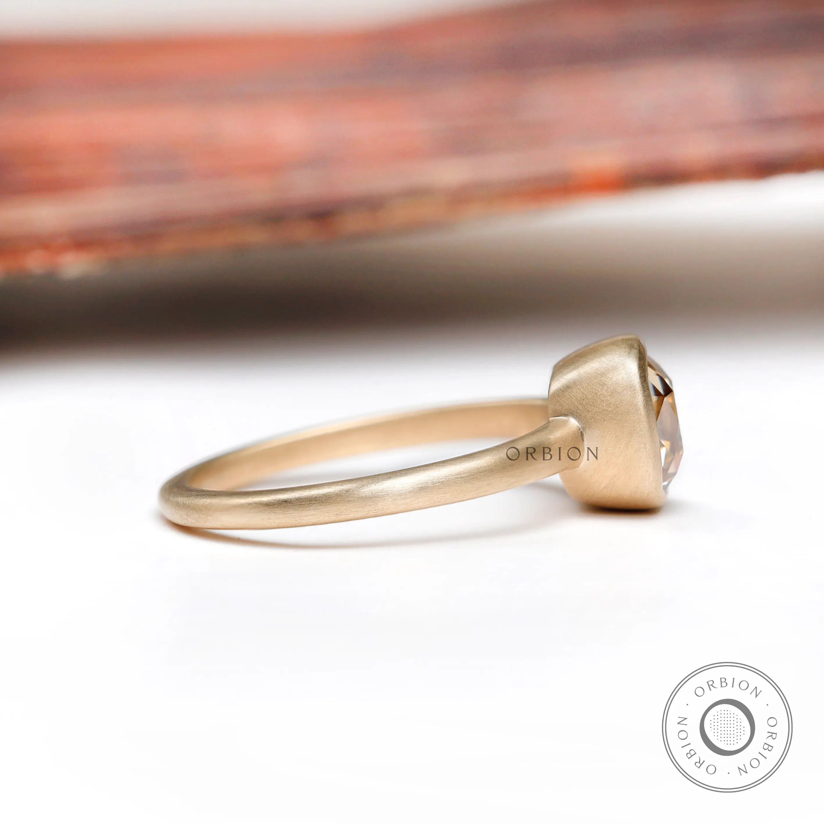 Side profile highlighting the bezel setting and matte 10K yellow gold band of the solitaire cushion cut dark champagne moissanite ring