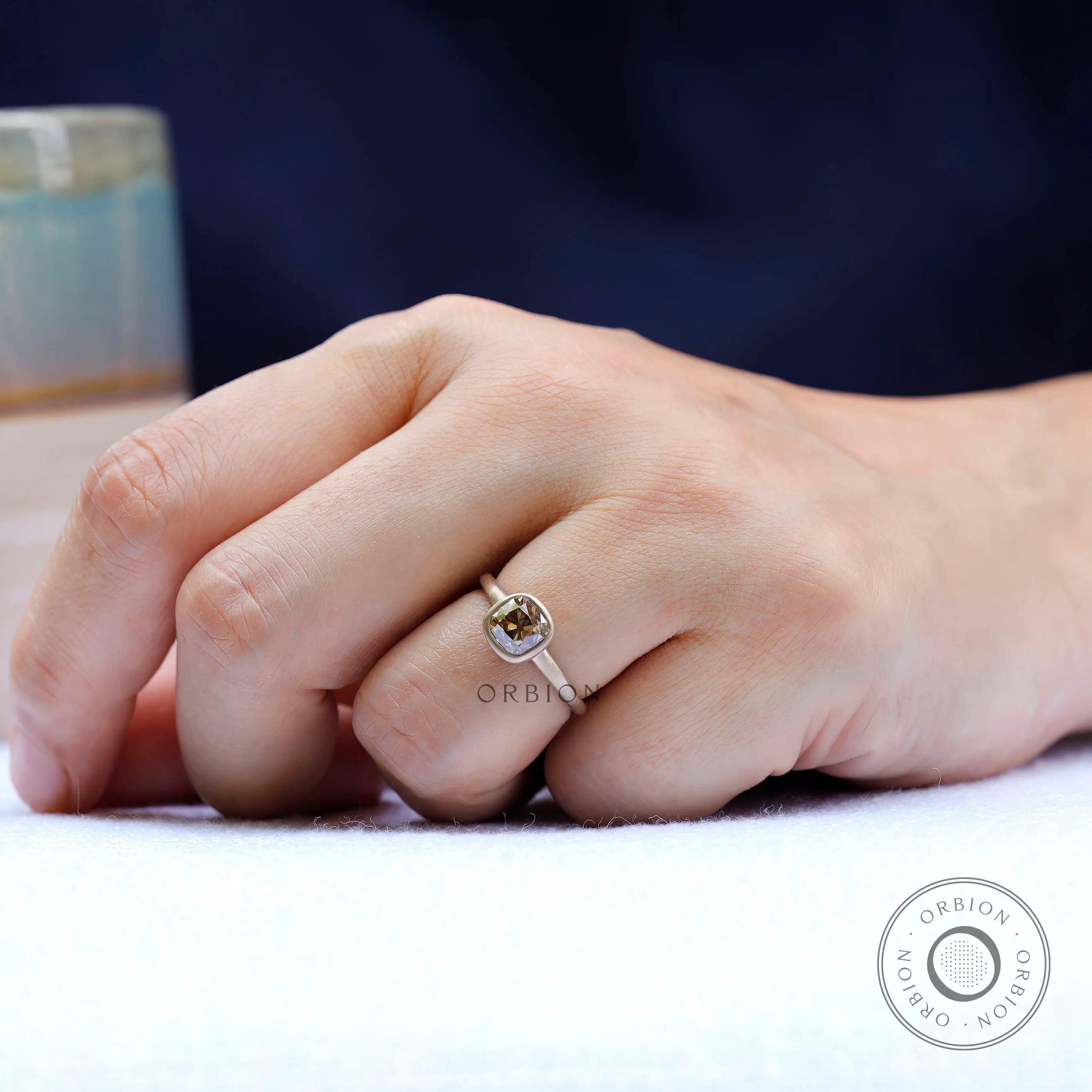 Solitaire cushion cut dark champagne moissanite engagement ring worn on hand