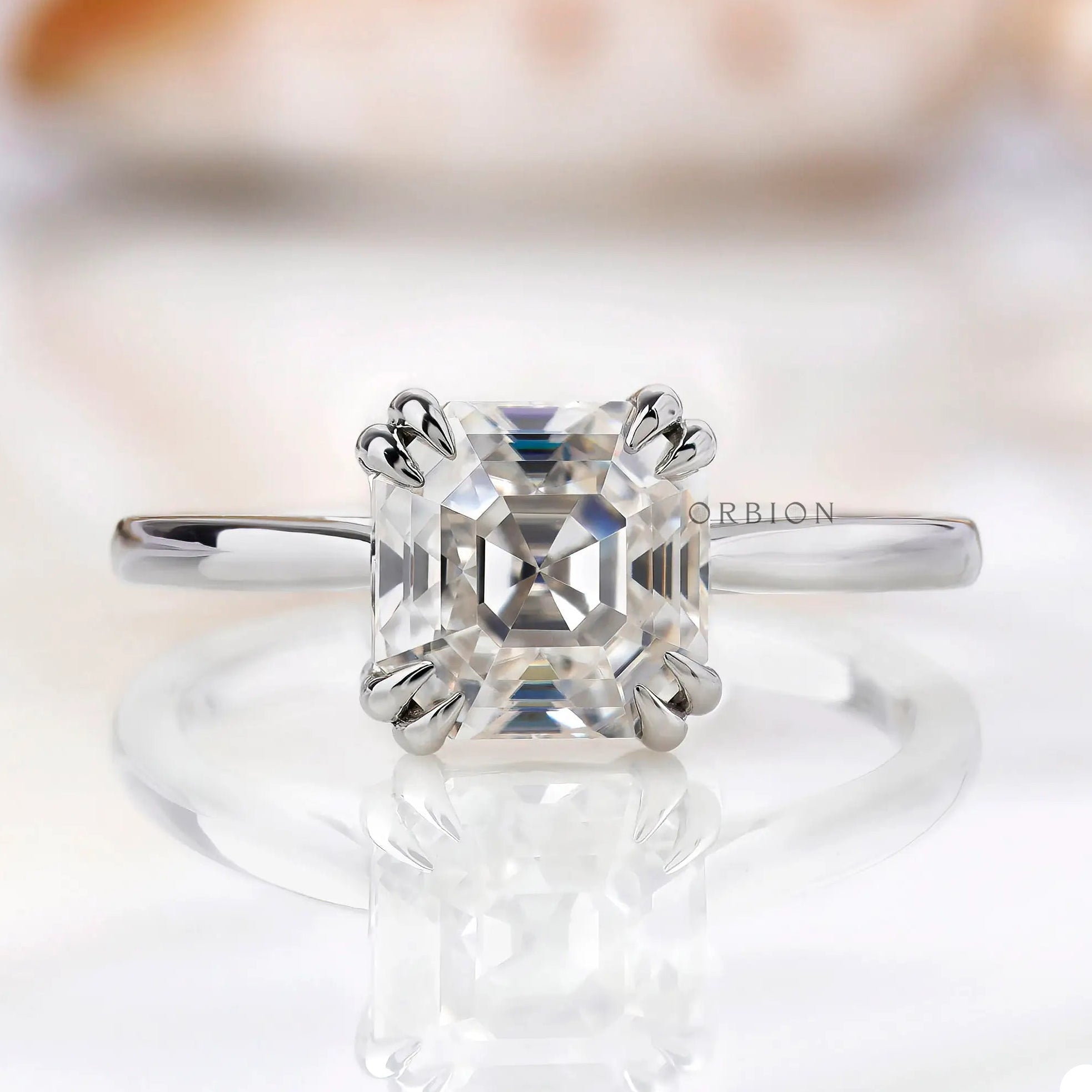 Asscher cut Moissanite solitaire ring on a white marble surface.