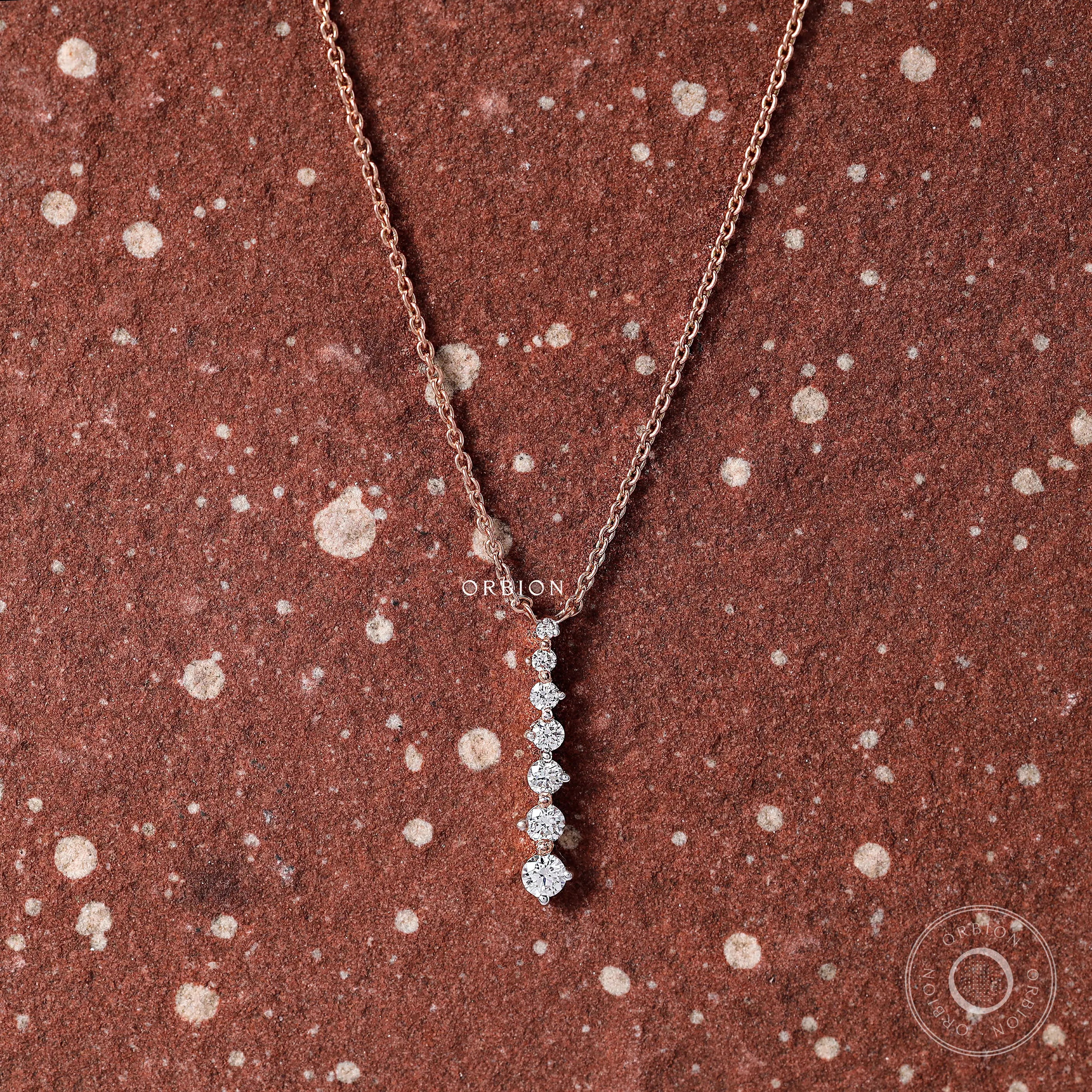 Close-up shot of a vertical drop pendant with graduated diamonds set in rose gold.