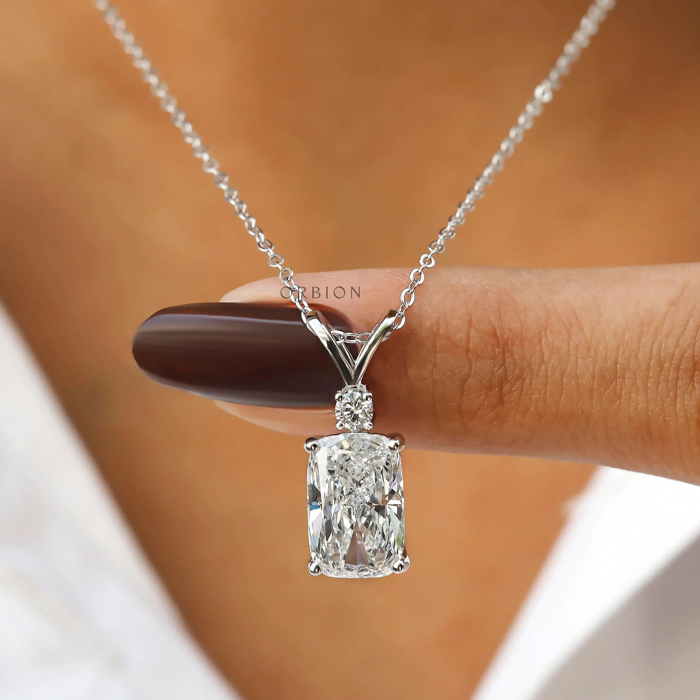 Finger held view of elongated cushion lab diamond pendant.