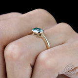 Minimal yellow gold engagement ring with blue green moissanite center stone