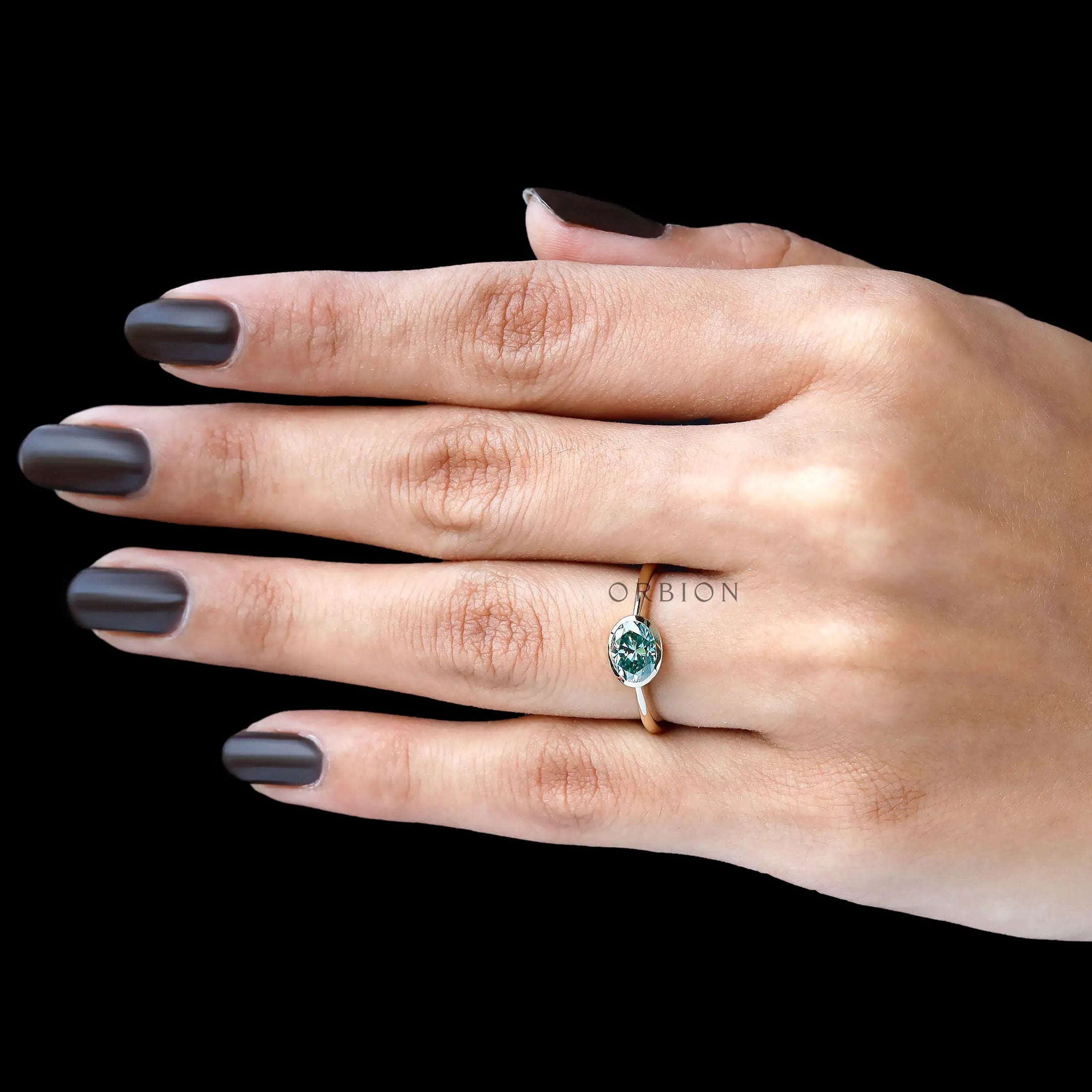 Hand model wearing blue green oval moissanite bezel engagement ring