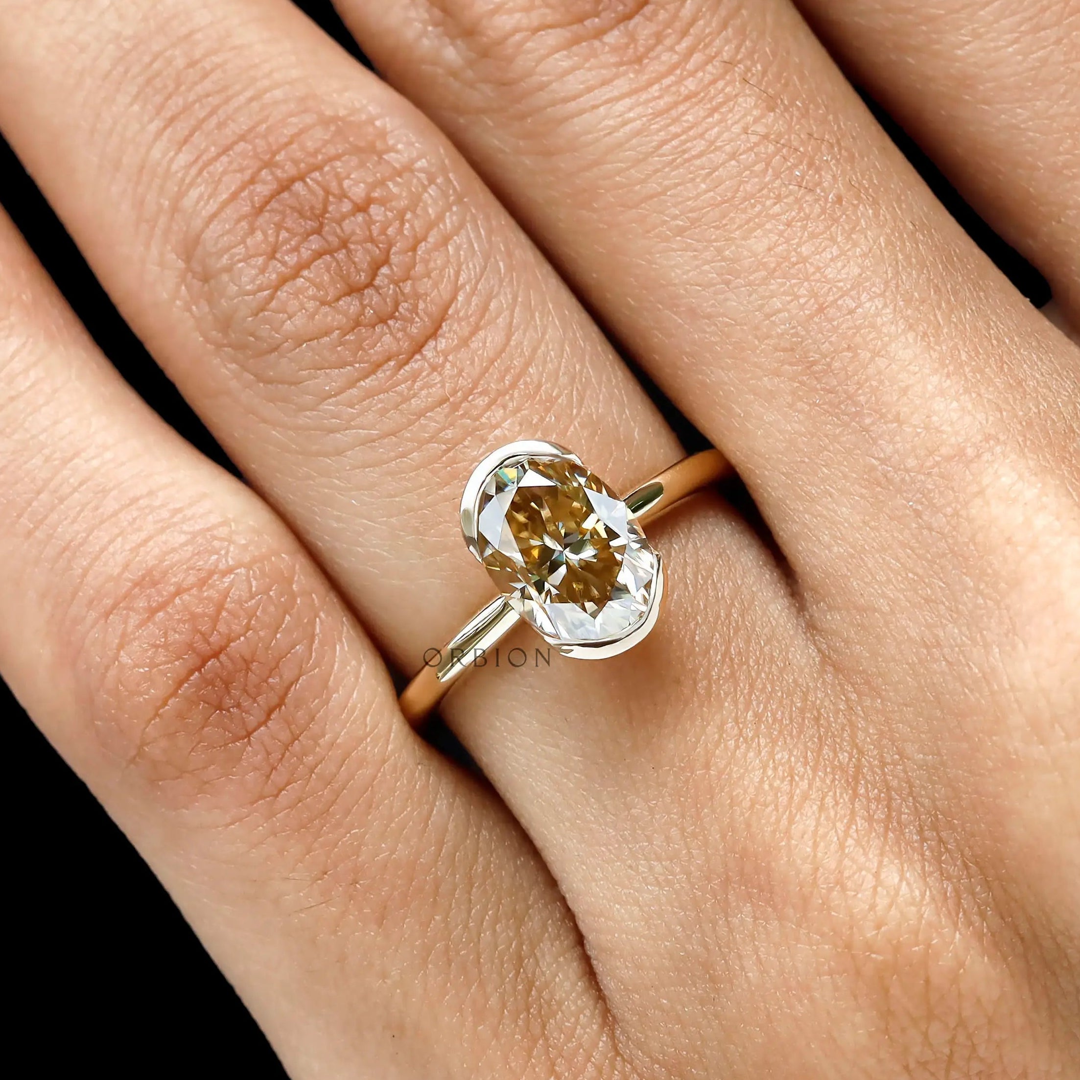 Closeup on hand highlighting oval moissanite and half bezel frame