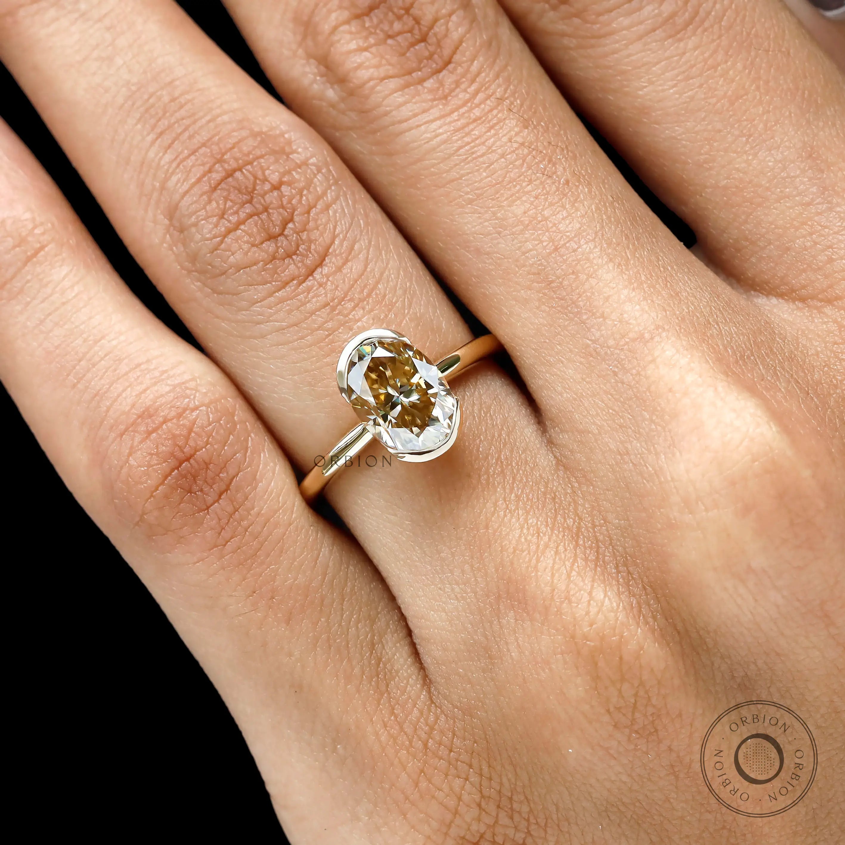 Closeup on hand highlighting oval moissanite and half bezel frame