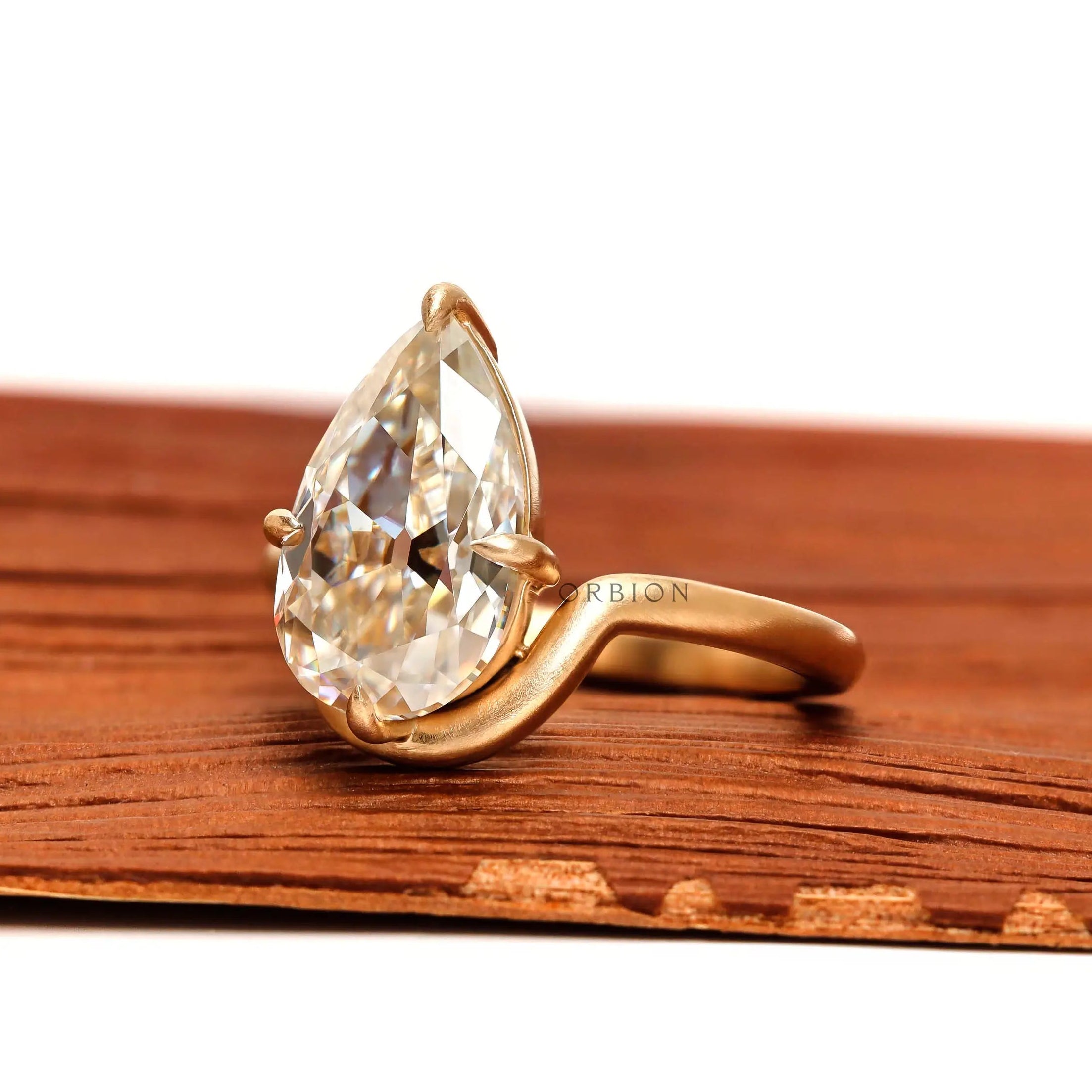Angled view pear moissanite bypass solitaire ring in brushed matte gold