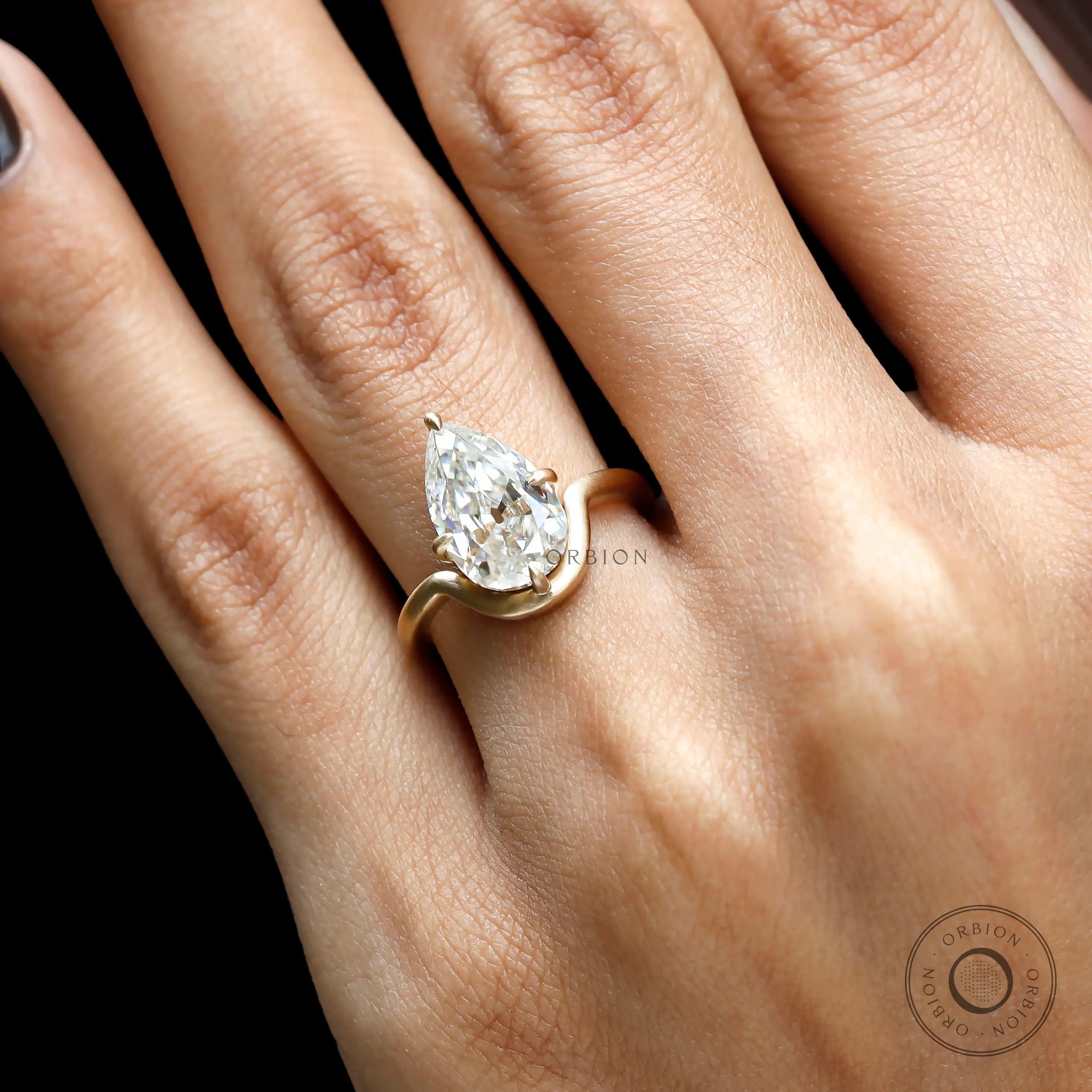 Close hand view pear moissanite bypass engagement ring in matte gold