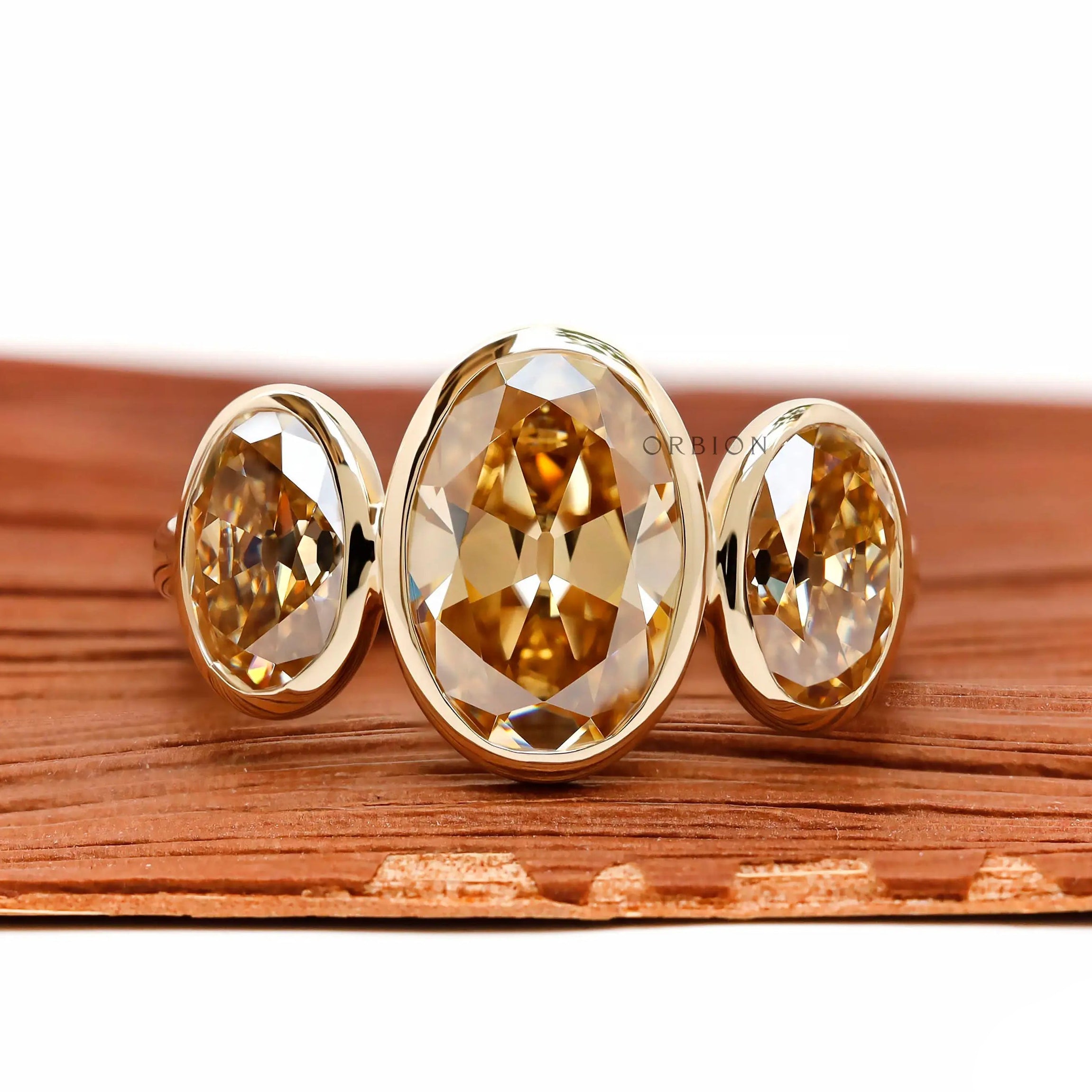 Front view three stone bezel set champagne oval moissanite ring.