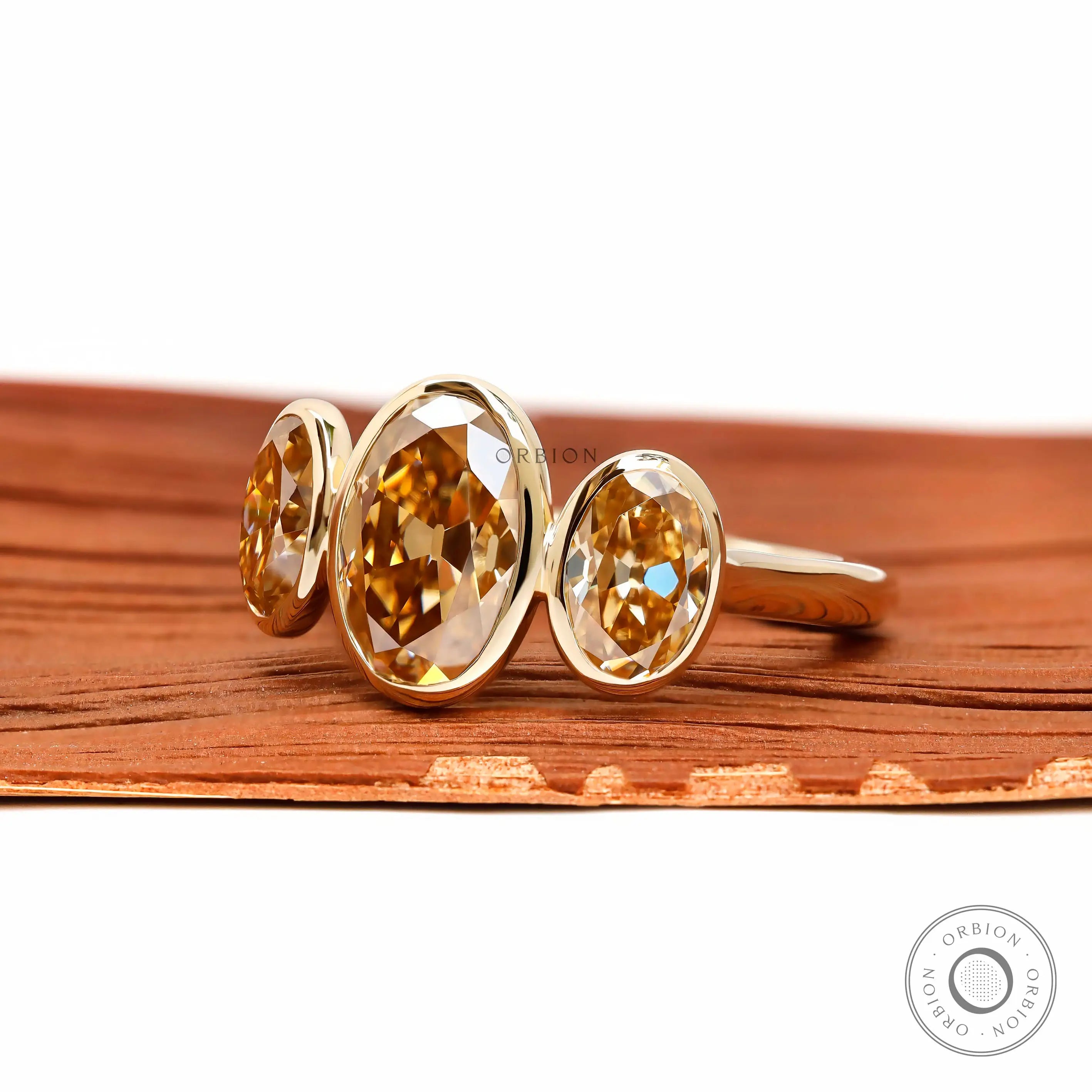 Angled front view of three stone oval bezel moissanite ring.