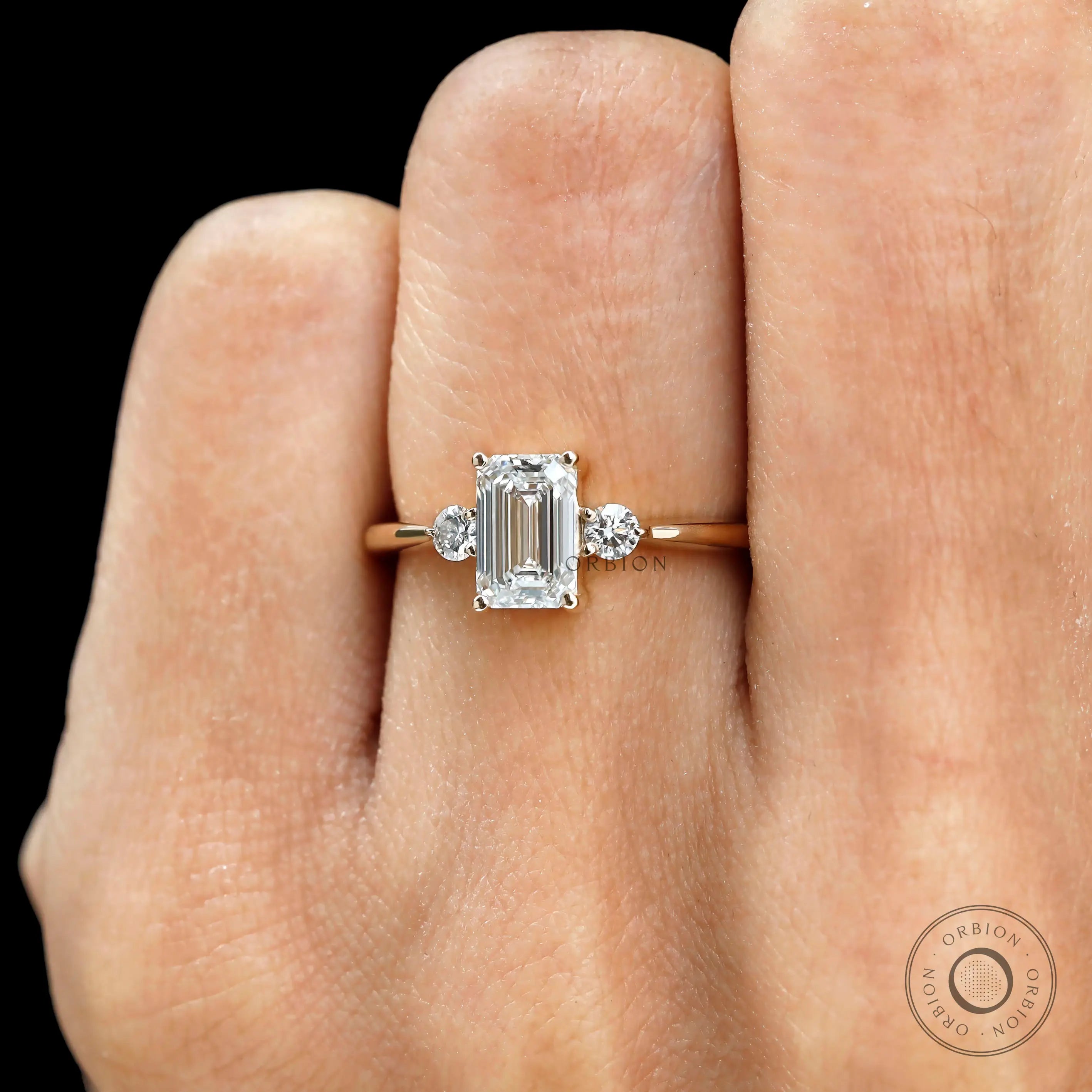 Delicate emerald cut engagement ring with round side stones on hand